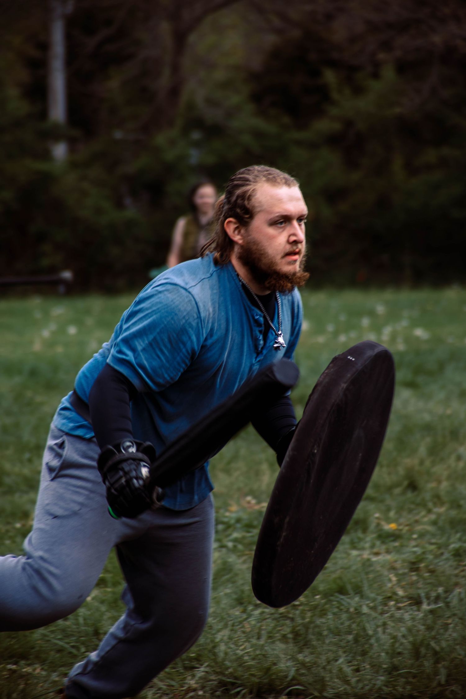 Person in blue shirt and gray pants performs dynamic exercises with a tire on grass field.