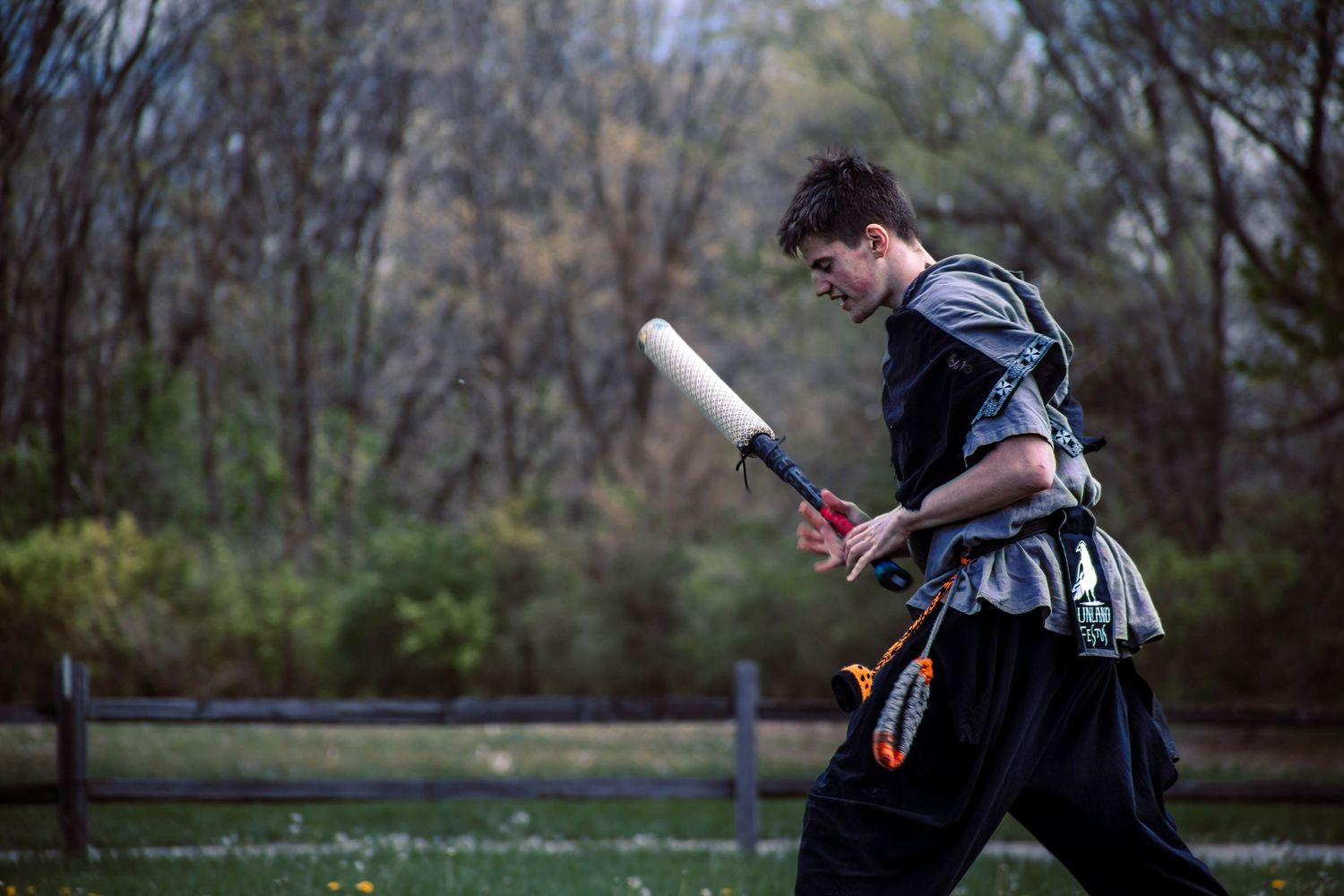 A person in a black jacket performs parkour moves and flips through a wooded outdoor area.