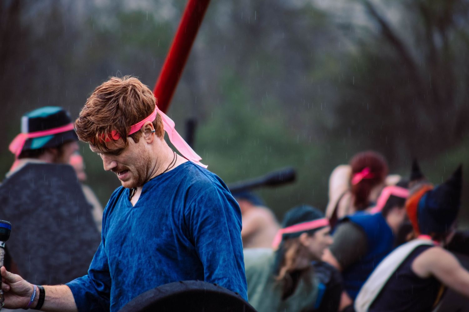 A group of people perform a historical reenactment battle scene with red and blue flags in an outdoor setting.