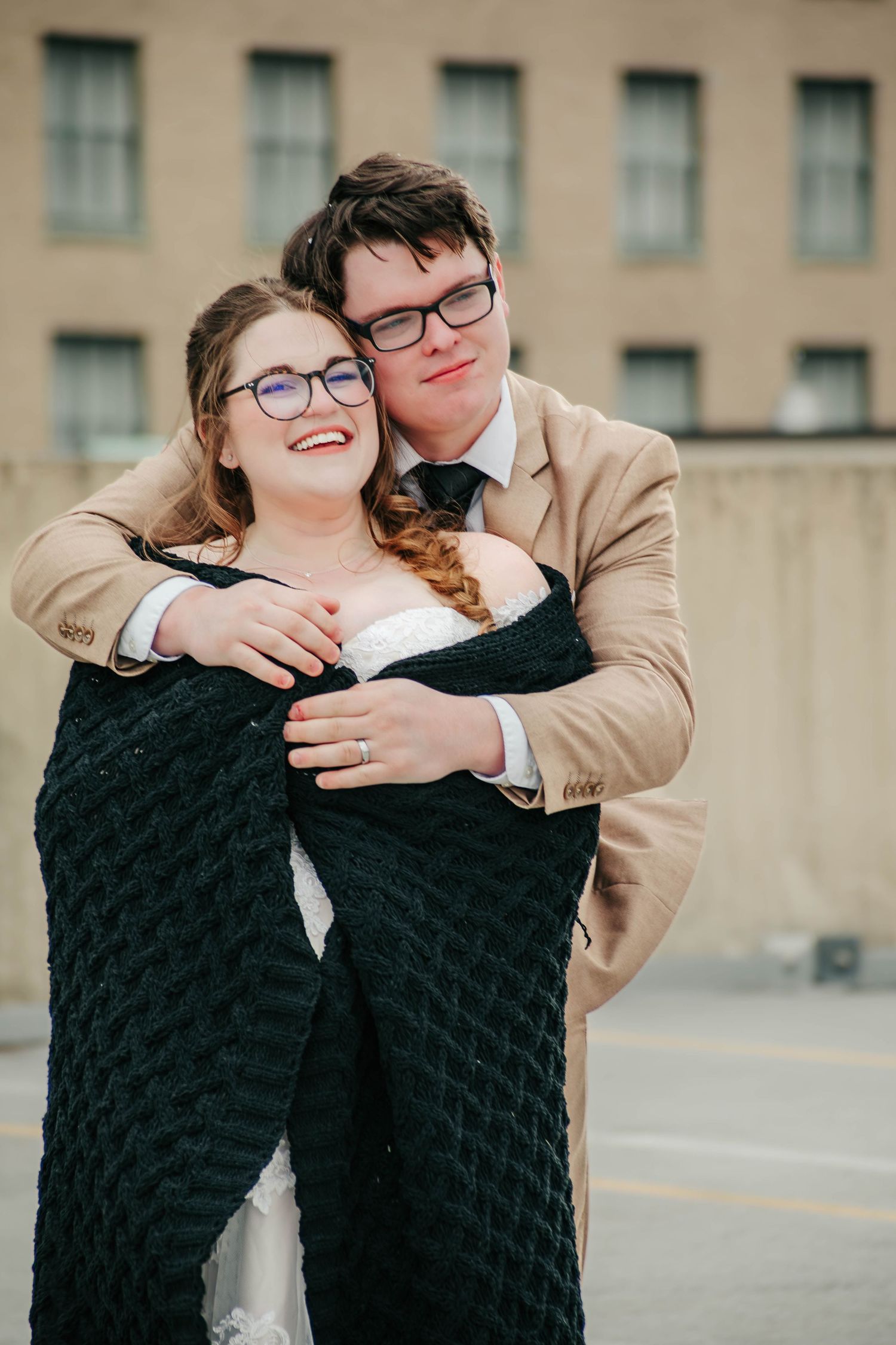 A couple in warm winter attire share an embrace against an urban backdrop.