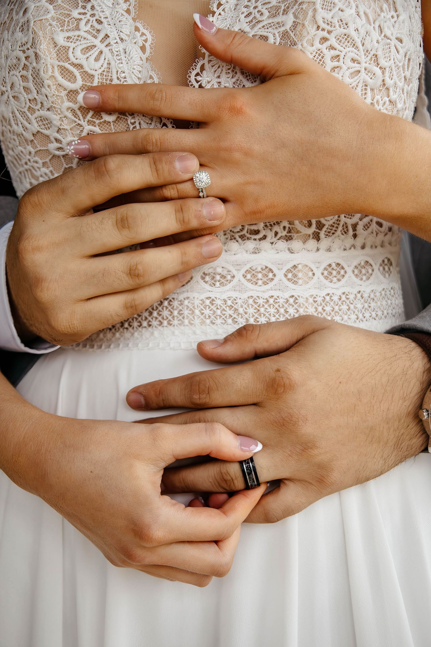 Close up of hands showing wedding rings against white lace dress detail.
