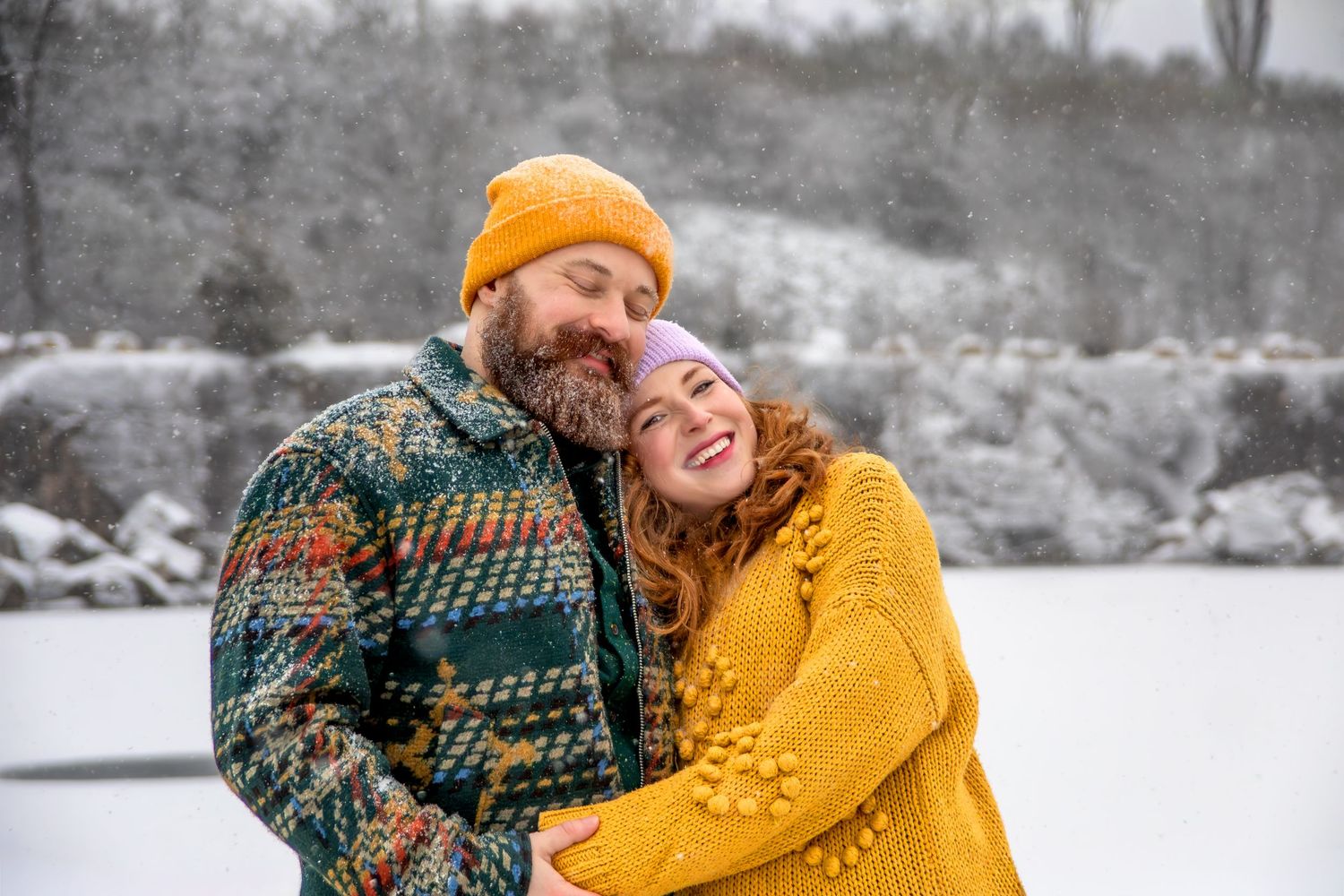 A couple in winter attire embraces and laughs together in a snowy outdoor setting.