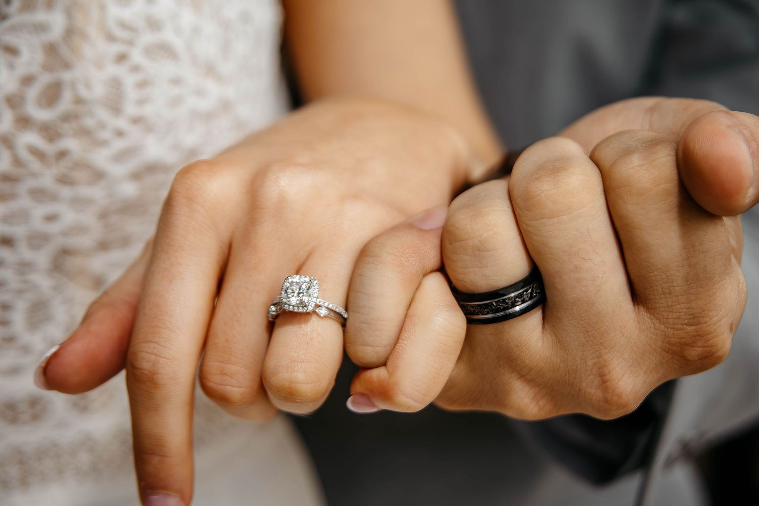 Close-up shot of two hands with wedding rings, showing a diamond engagement ring and black band.