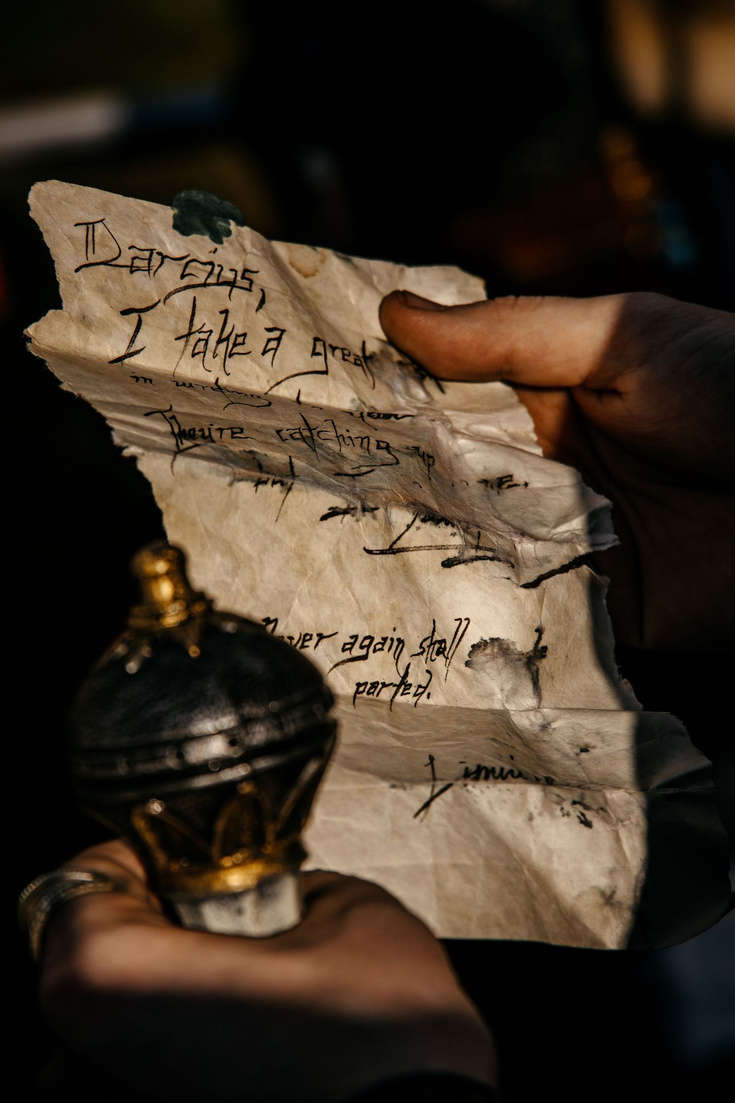 Hands holding an aged, crumpled letter with handwritten text next to a vintage ornate ink bottle.