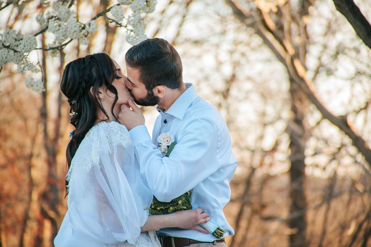 Romantic autumn wedding photo of couple sharing a tender kiss among fall foliage.