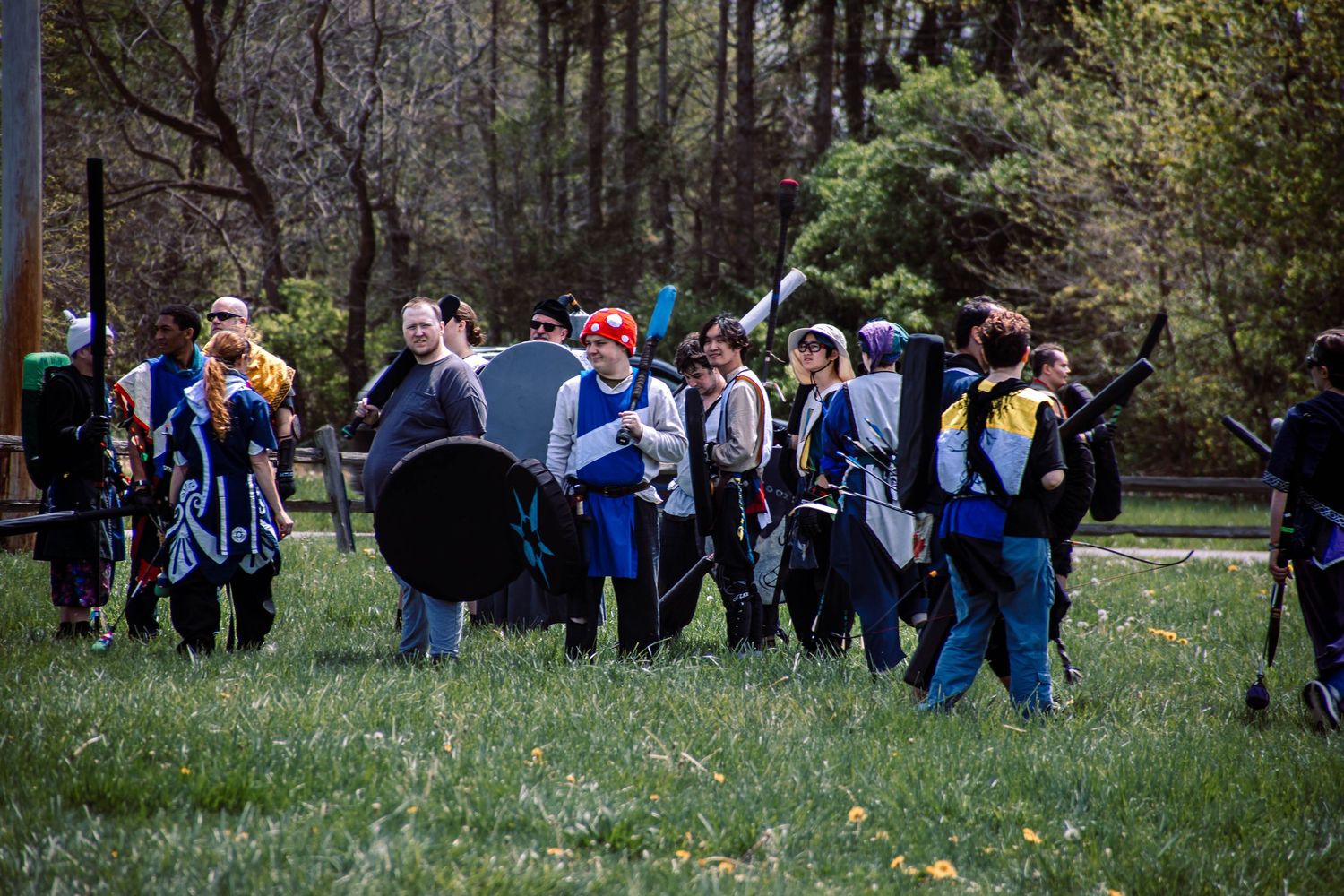 A group of people in blue costumes gather in a grassy field during what appears to be a medieval reenactment event.