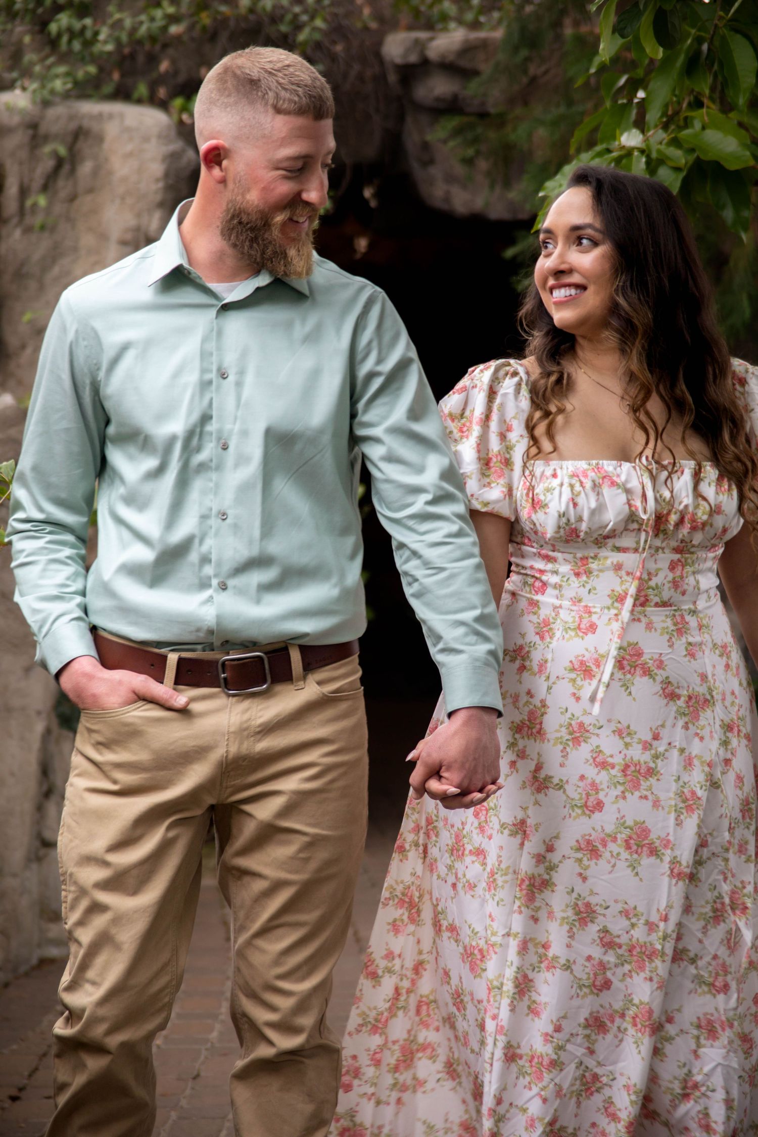 Couple in spring attire posing together against stone wall, showing casual intimacy.