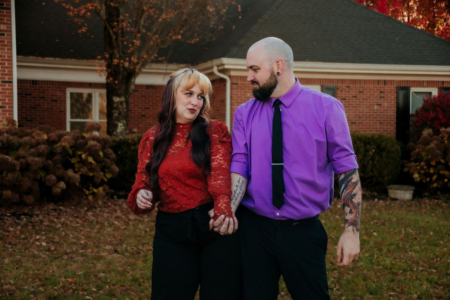 A couple in purple and red outfits shares playful moments against bright autumn foliage.