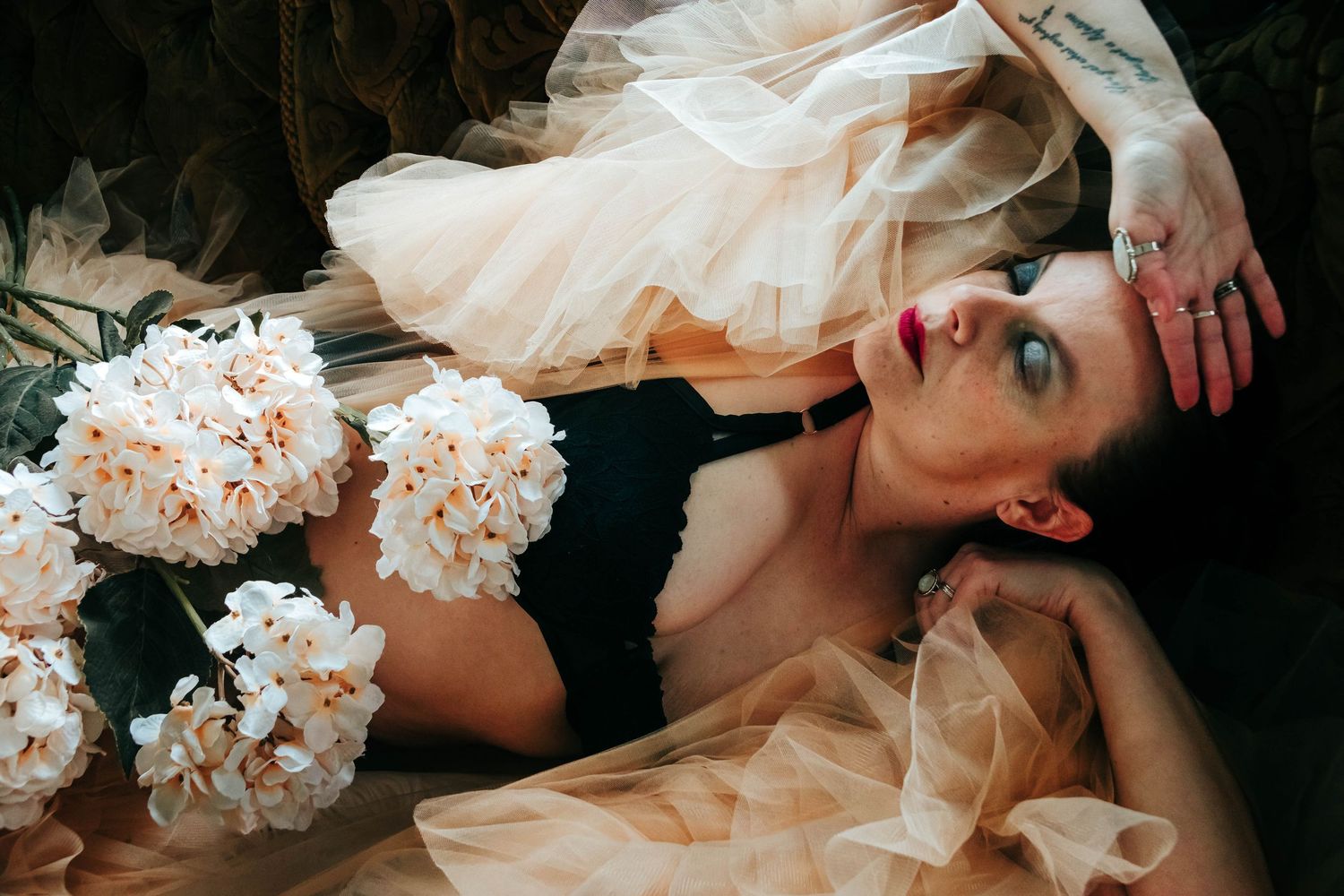 Artistic boudoir photo with peach tulle fabric and white floral bouquets creating a romantic mood.