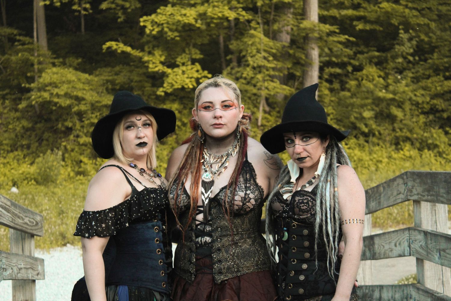 People dressed in dark gothic clothing stand together against a wooded backdrop.