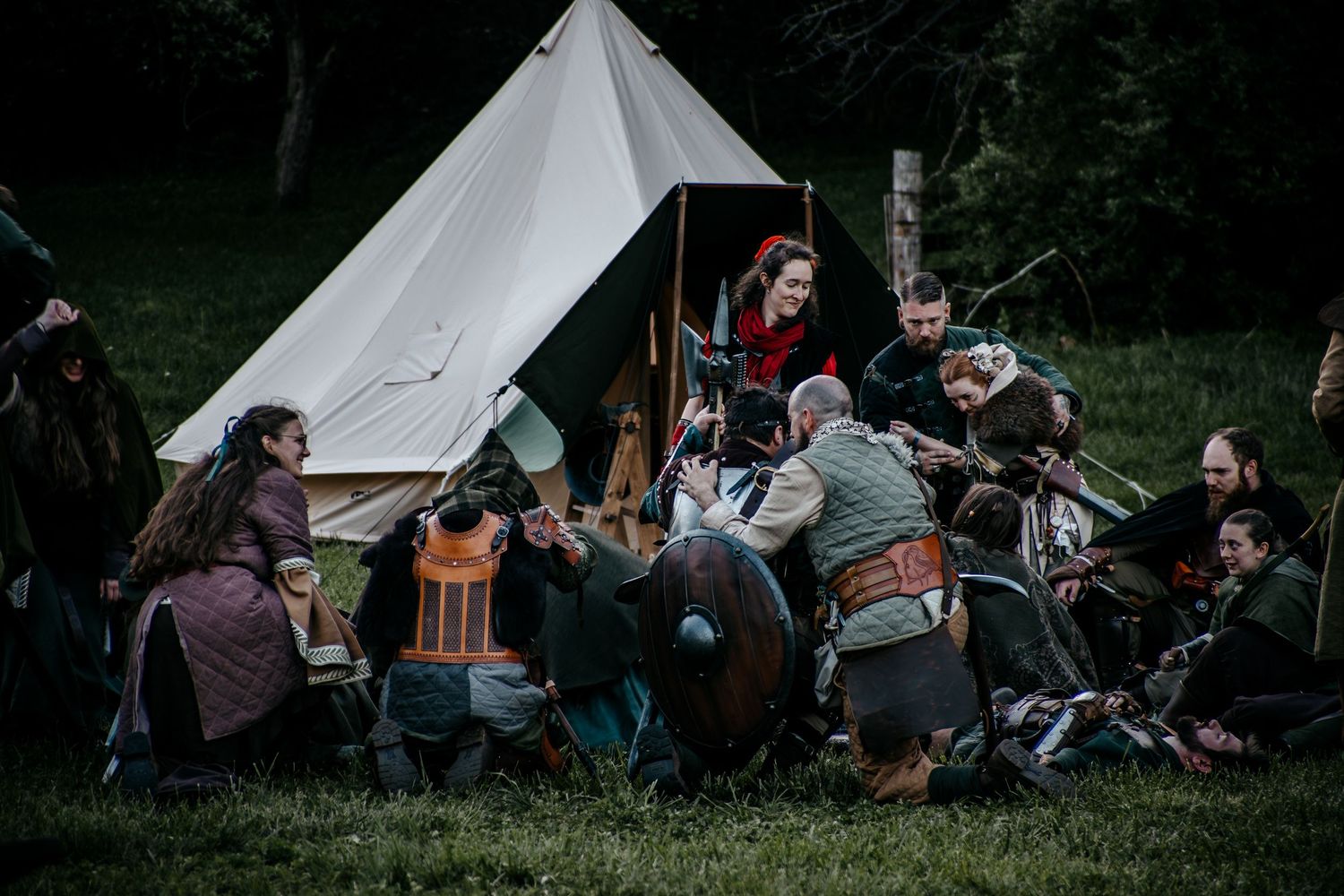 Medieval Viking reenactment group gathered around a white canvas tent in a forest clearing, wearing historical costumes.