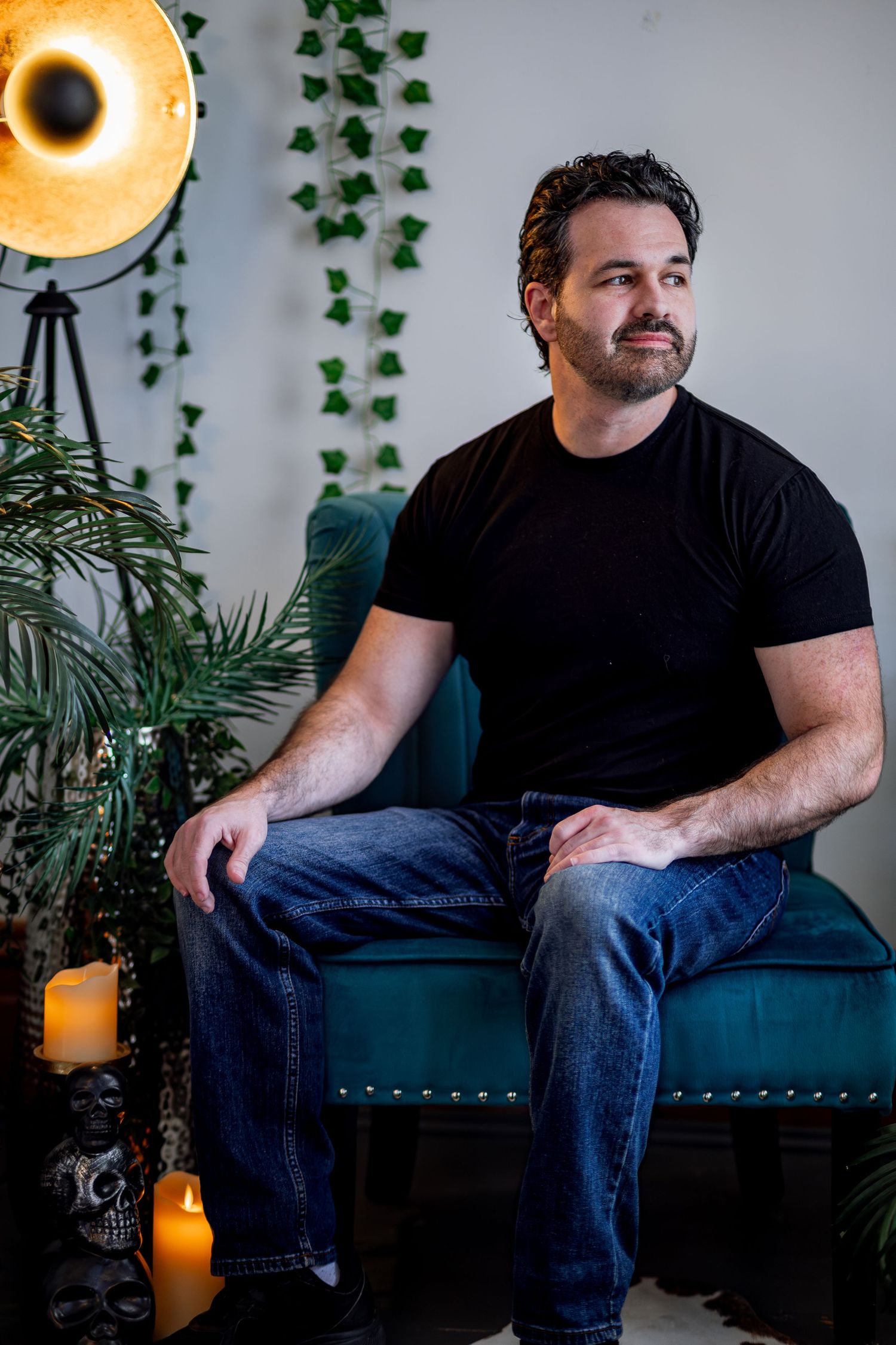 Person in black shirt and jeans sits on blue bench with warm lighting and plants in background.