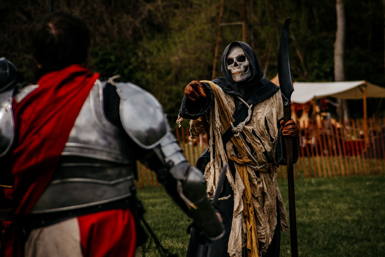 Grim Reaper costume confronts a medieval knight at a Renaissance faire outdoor event.