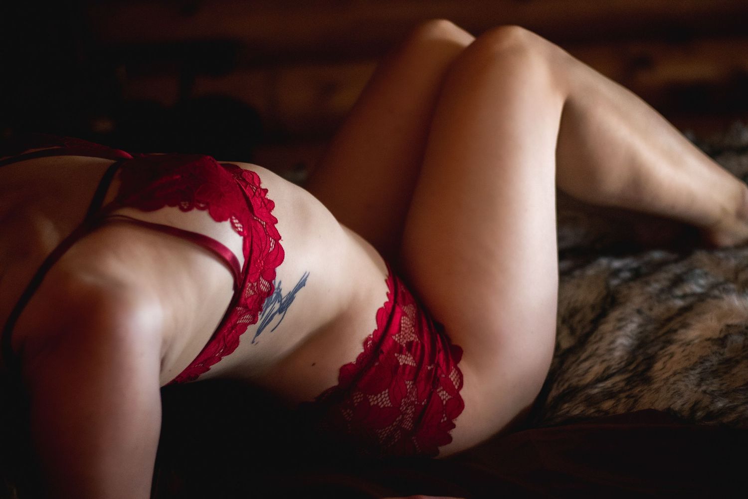 Close up view of red lace lingerie details against dark textured background.