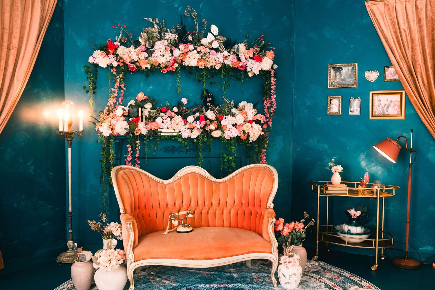 A vintage-style photography studio with teal walls, coral pink sofa, and cherry blossom floral decorations.