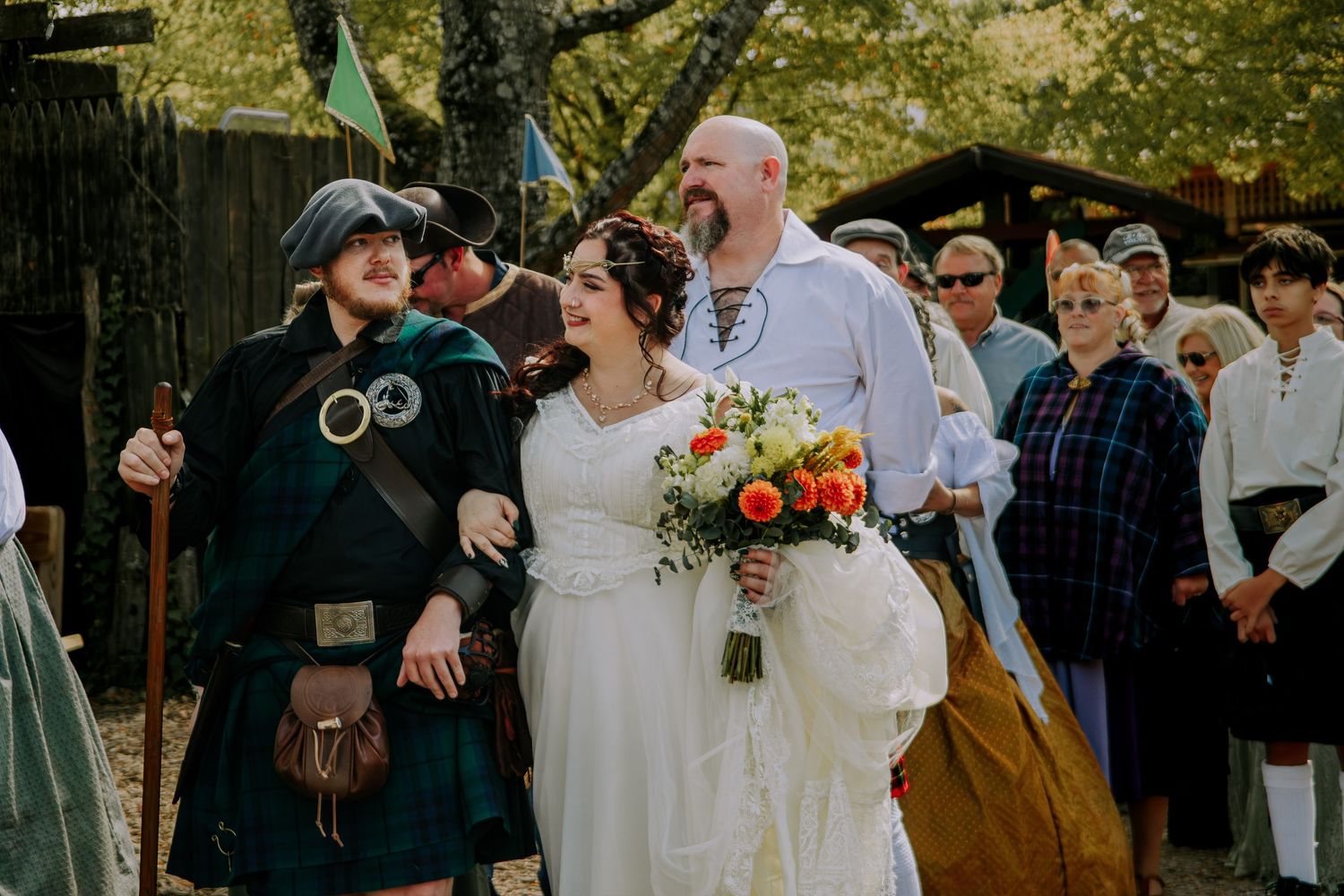 Bride and groom smile joyfully at Renaissance faire wedding ceremony, surrounded by guests in medieval costumes.