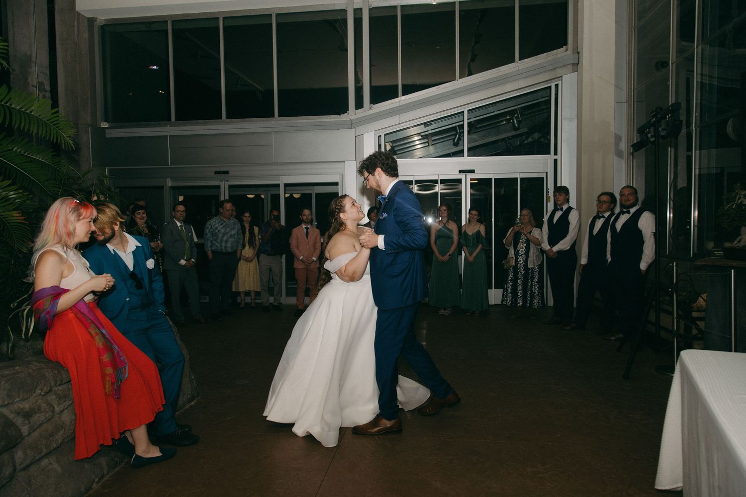 Bride and groom share their first dance at indoor wedding reception surrounded by guests watching.