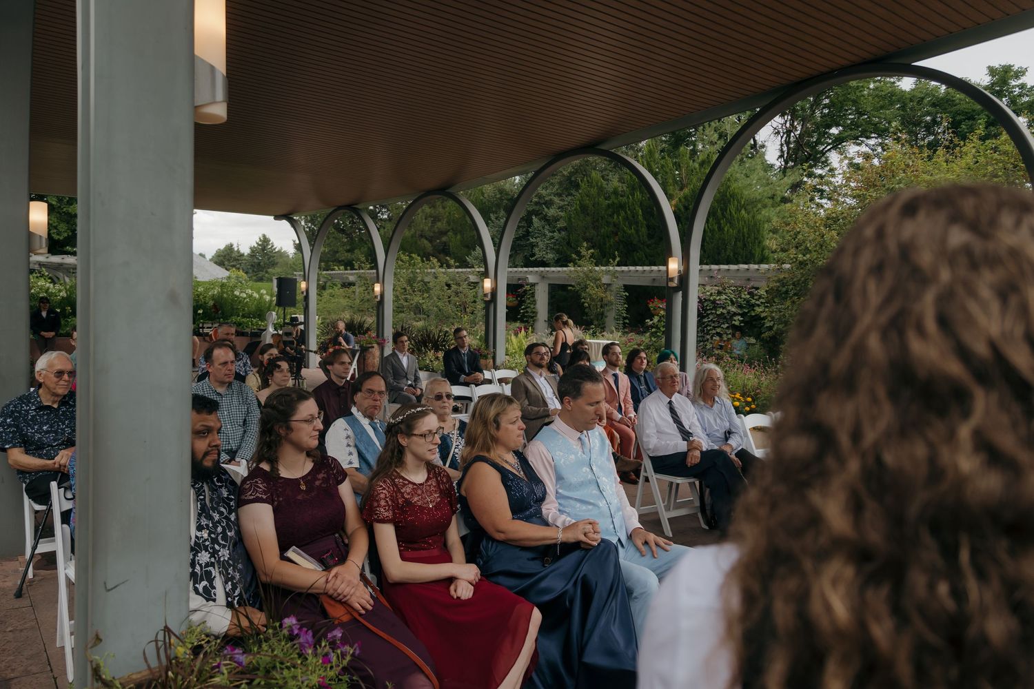 Guests seated under an elegant outdoor pavilion during a garden wedding ceremony surrounded by lush greenery.