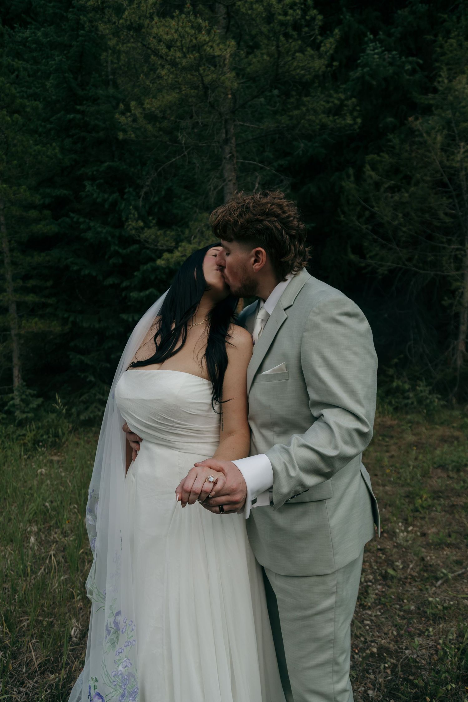 Bride and groom share romantic kiss in forest during intimate outdoor elopement ceremony.
