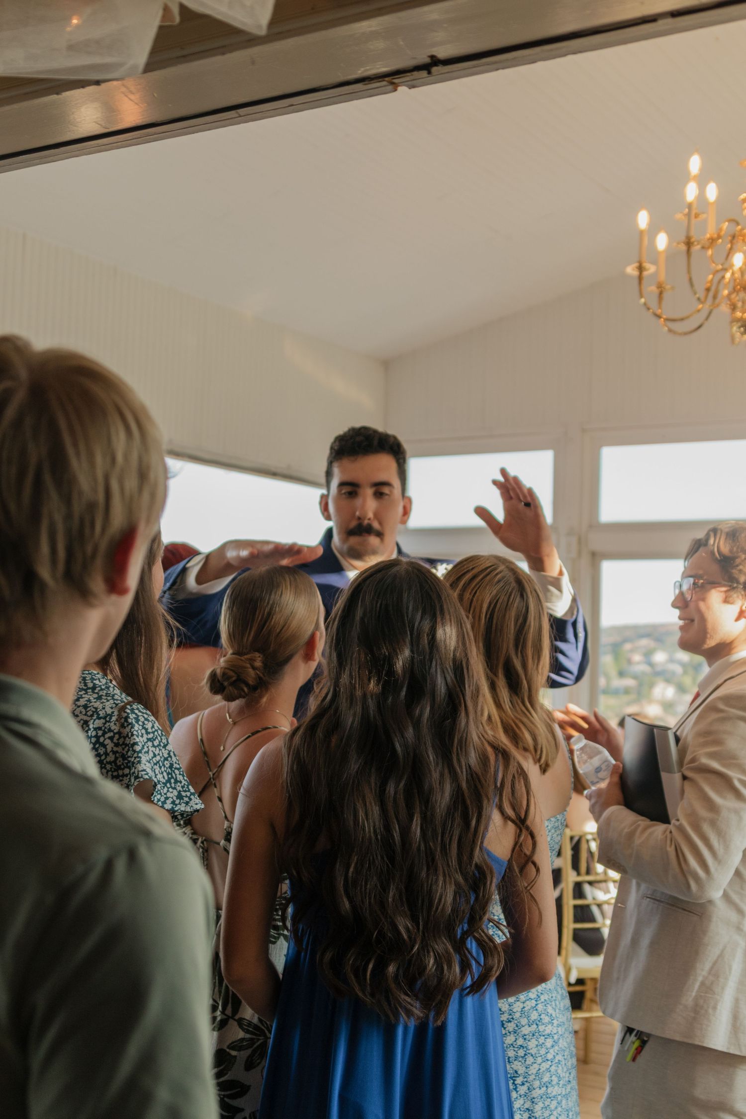 Wedding reception guests dancing and celebrating in a bright indoor venue with chandeliers.