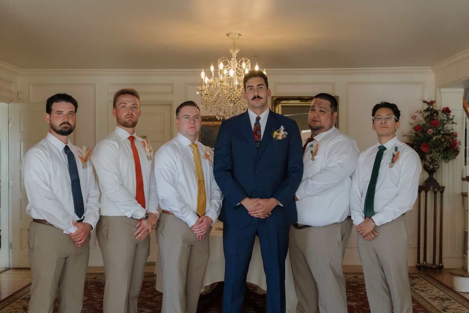 Wedding party in formal attire gathered for photos in an elegant indoor venue.