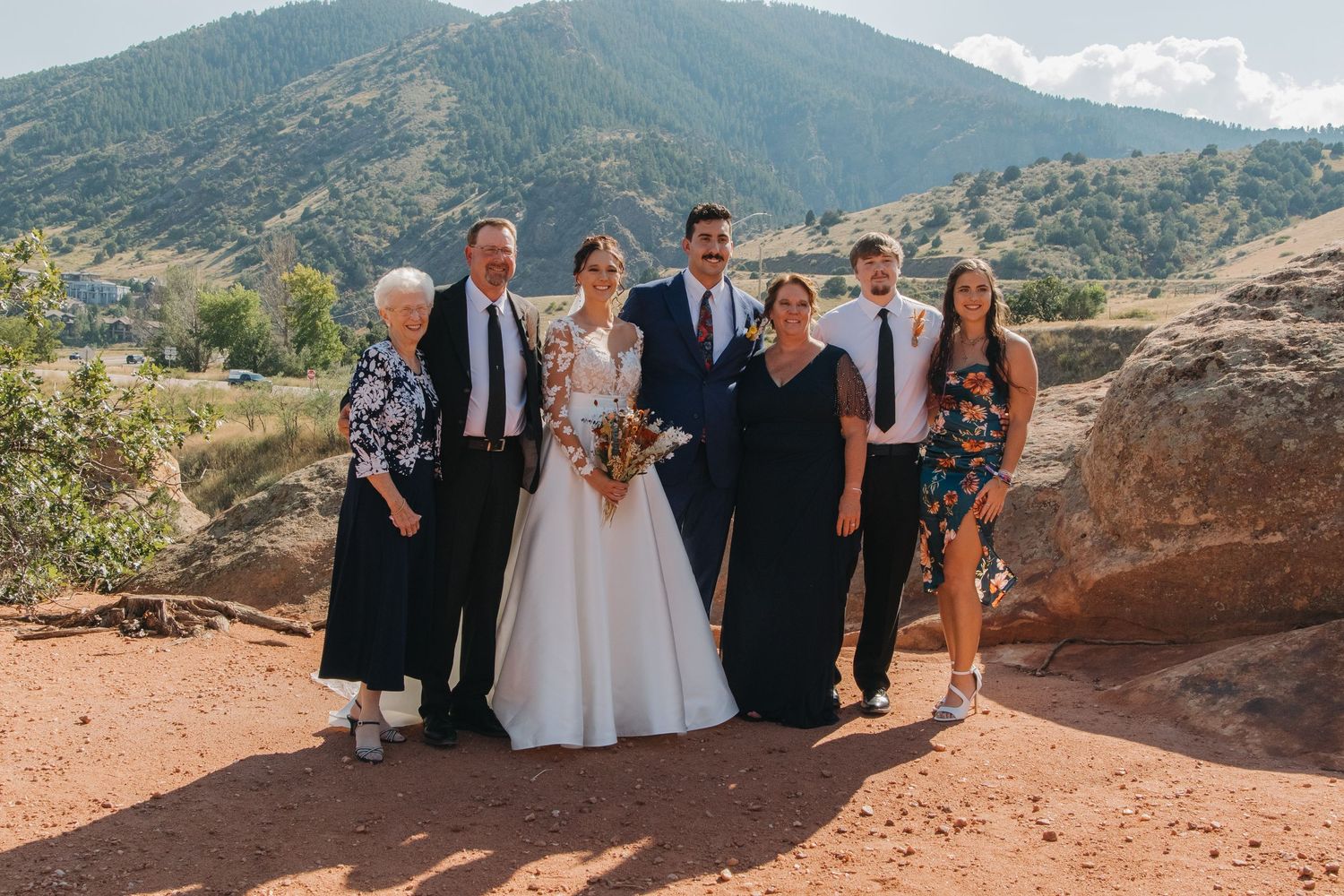 A wedding party poses together on red rocks with mountains in the background.