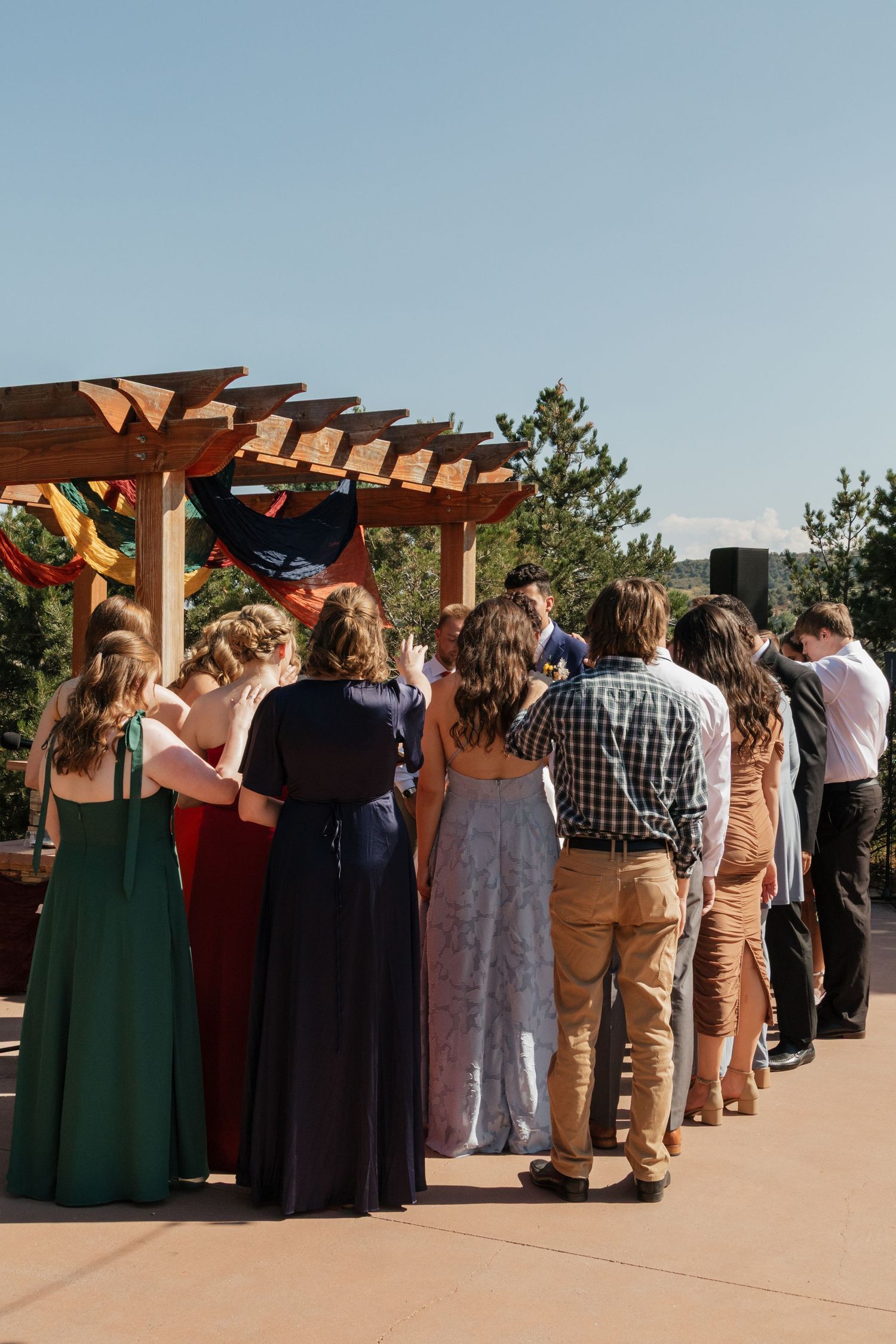 Wedding guests gathered under a wooden pergola for an outdoor ceremony.