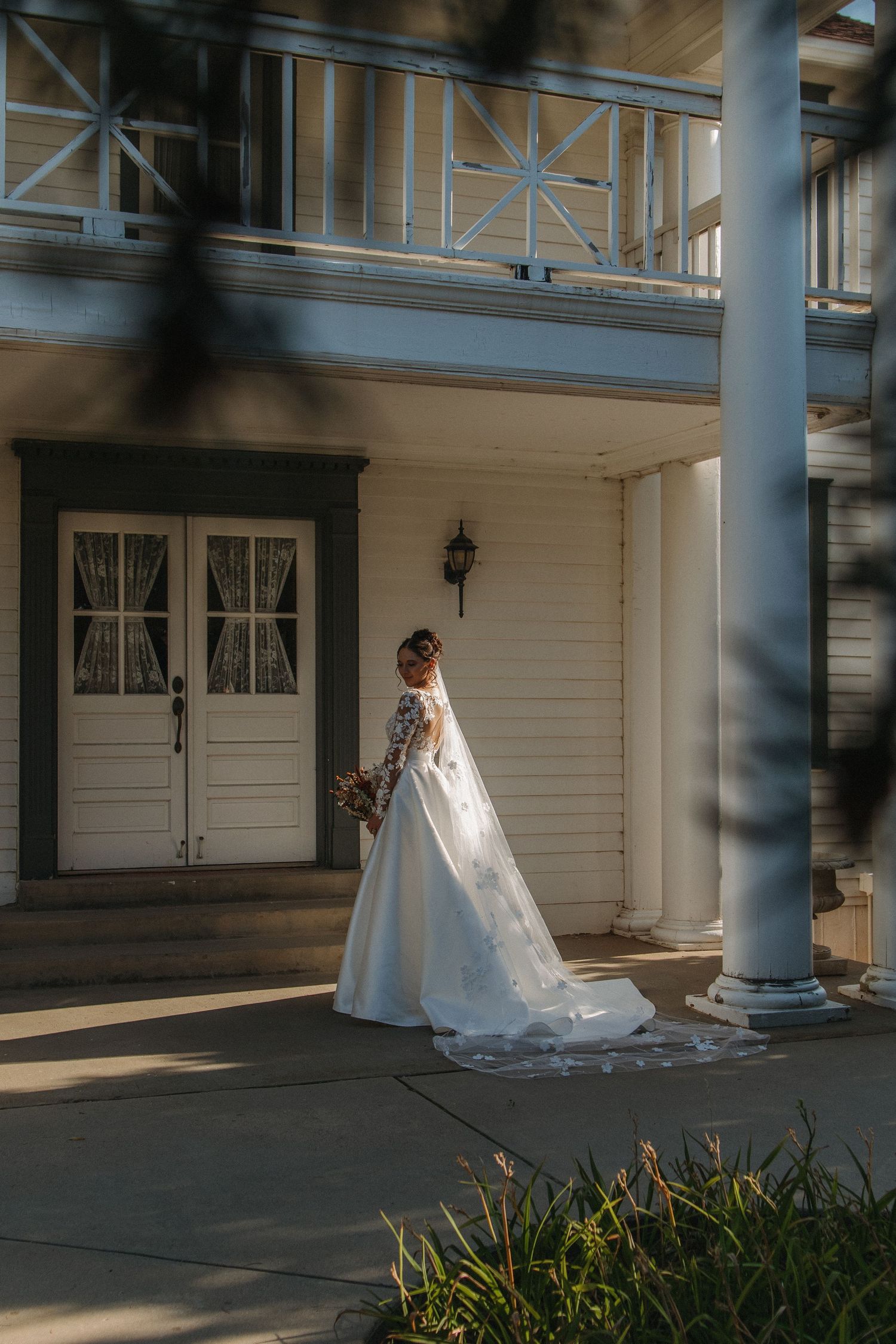 White wedding dress trailing along a covered porch of a classic white colonial building.
