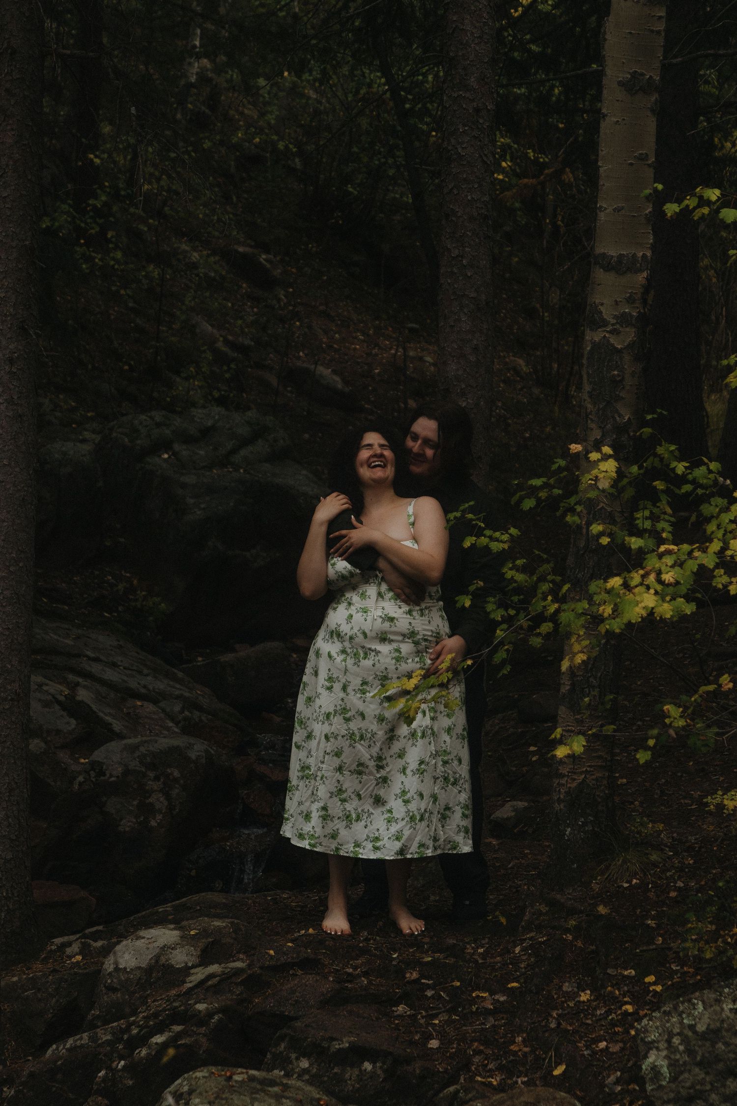 A series of forest photos shows a figure in a floral dress sitting among dark trees and fallen leaves during autumn.