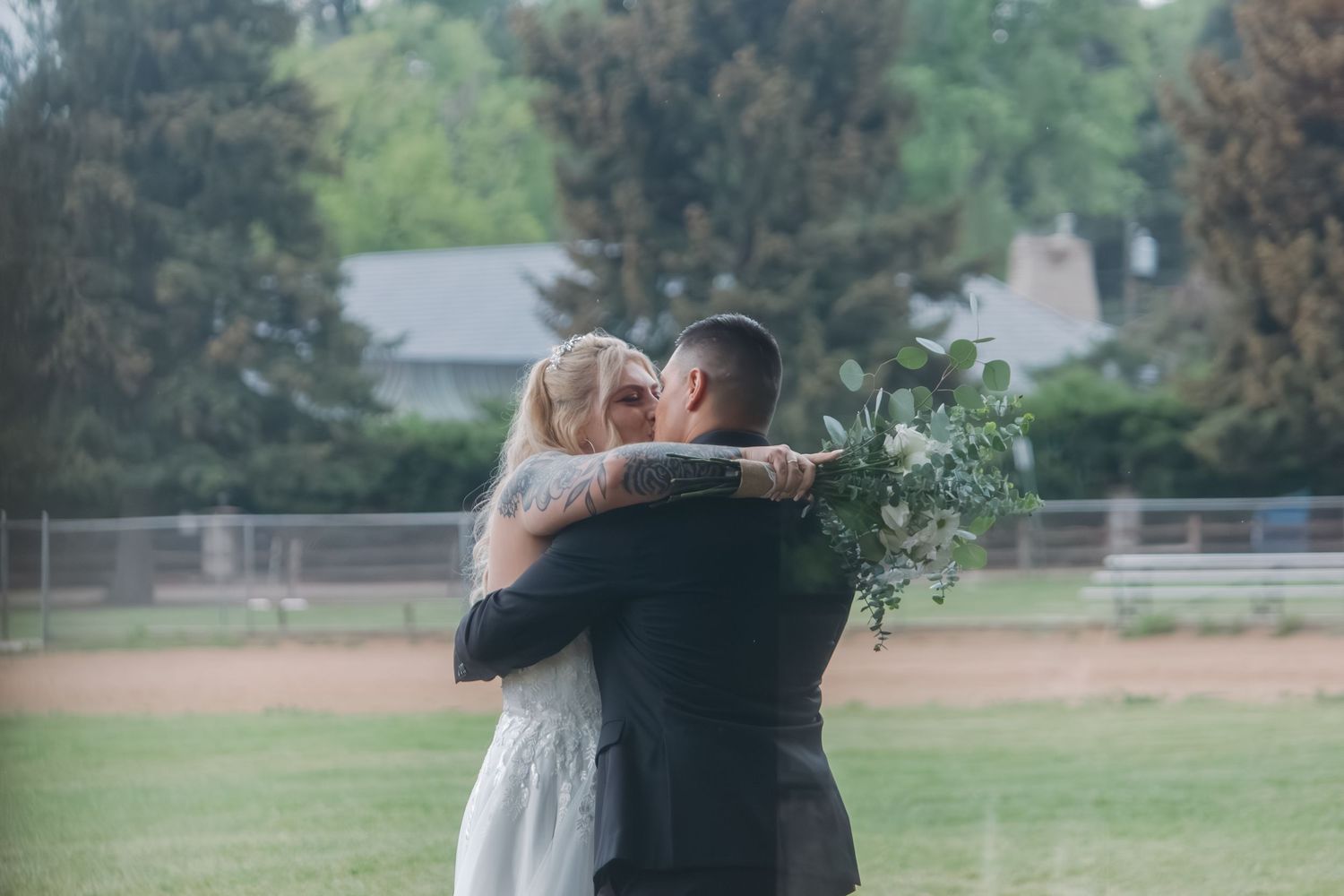 A couple embraces in an outdoor field while holding a floral bouquet.