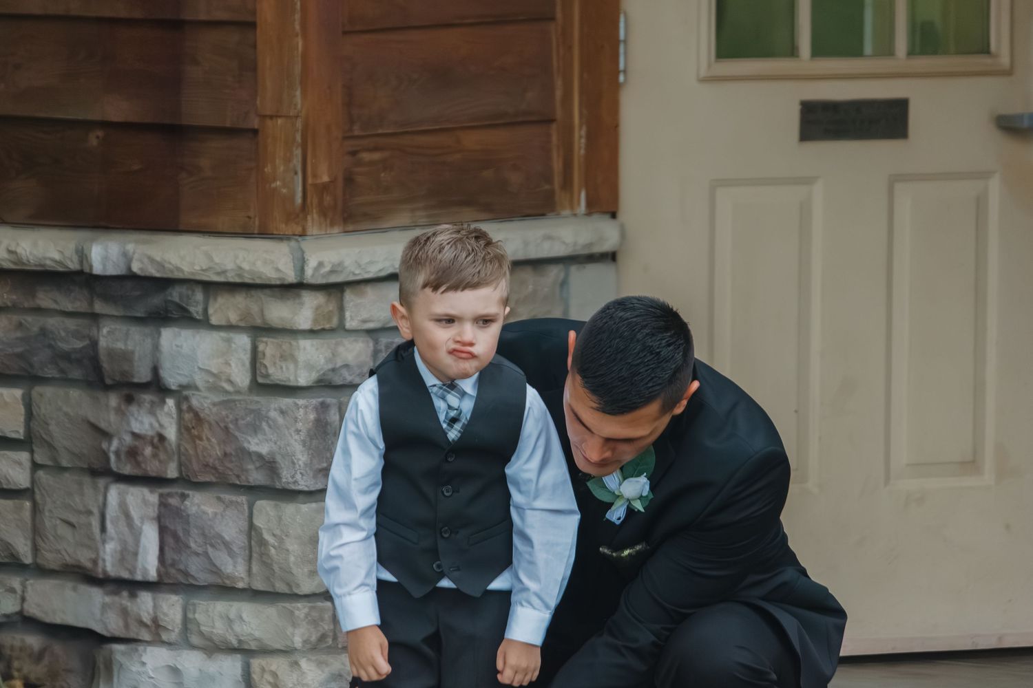 Small child in formal attire being helped with their shoes near a stone building entrance.