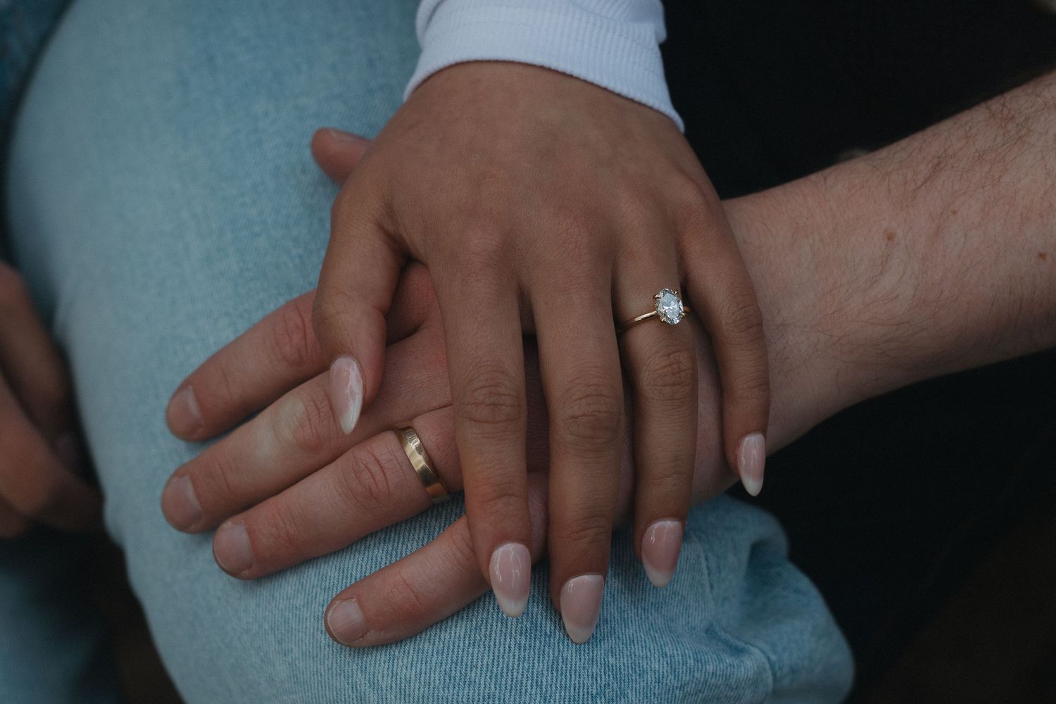 Close-up of hands with engagement rings intertwined against blue fabric.