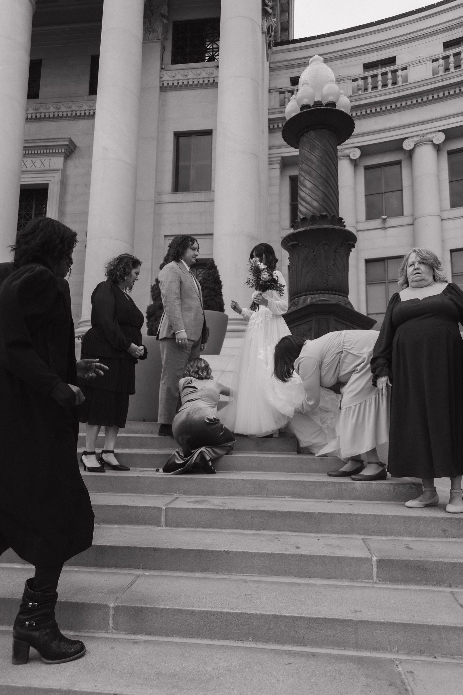 People sitting on white marble steps of a grand building with classical columns in black and white.