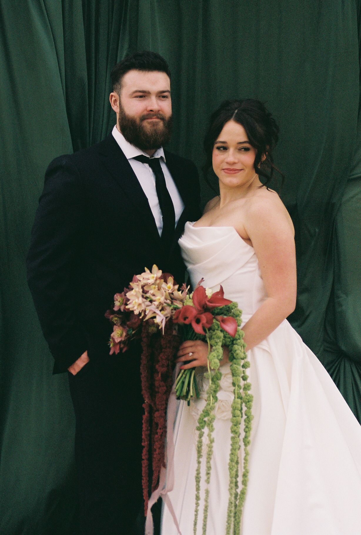 A formal wedding portrait against a deep green backdrop with a stunning bouquet featuring trailing elements.