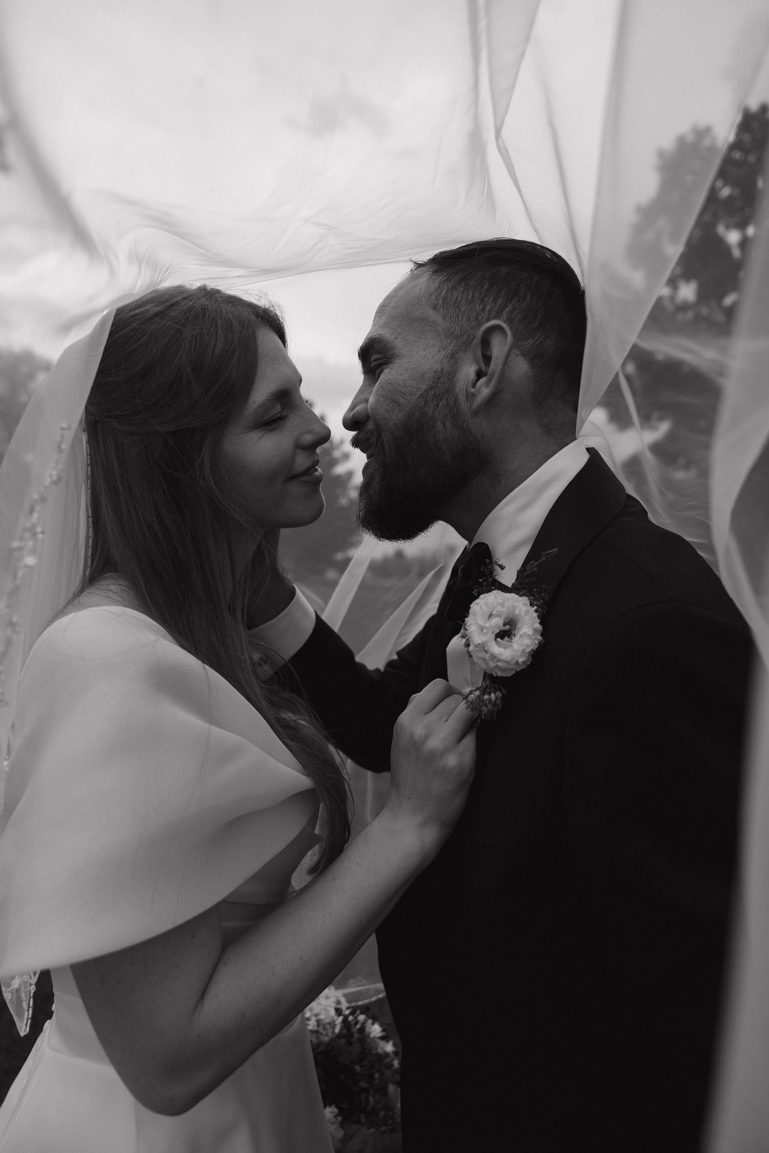 Black and white photo of bride and groom sharing romantic moment under wedding veil.