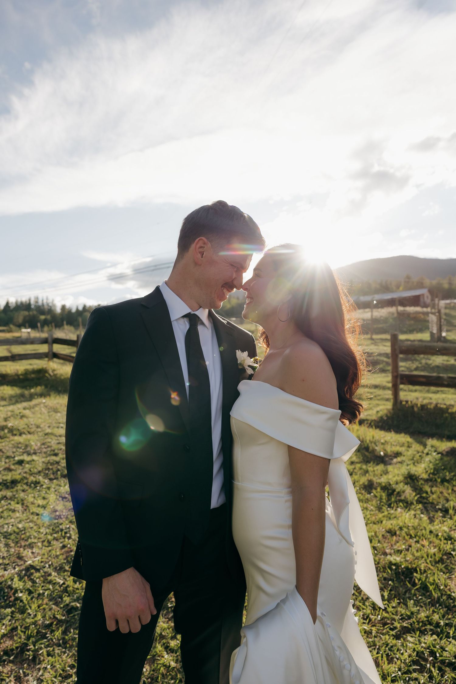 Bride and groom touching foreheads in golden sunlight at outdoor farm venue.