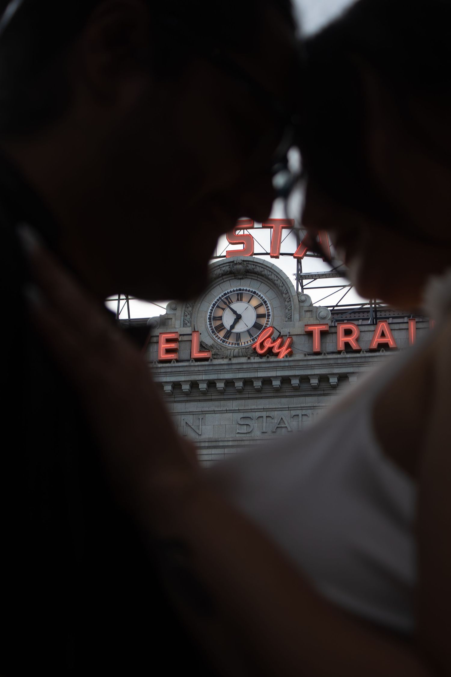 Illuminated vintage clock and signage at a train station captured through a moody, dark framed perspective.