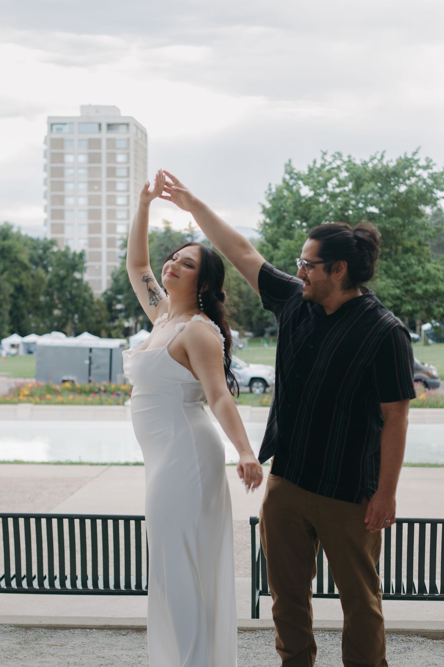 A playful dance scene captured outdoors with urban buildings and benches in the background.