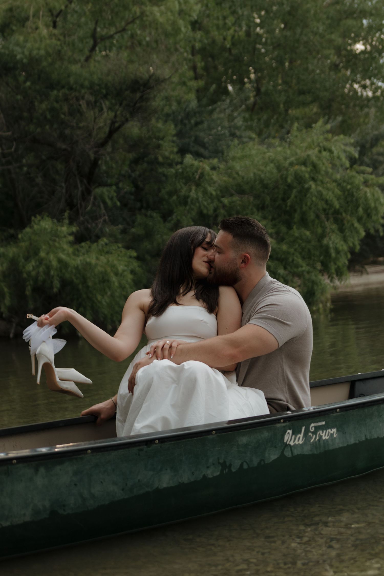 Tender moment between couple in traditional wedding attire sitting closely in a canoe.
