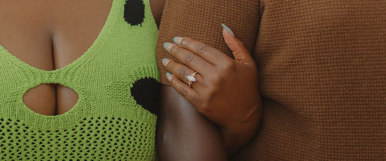 Dark-skinned person wearing a green ribbed sweater holds hands together against a neutral background.