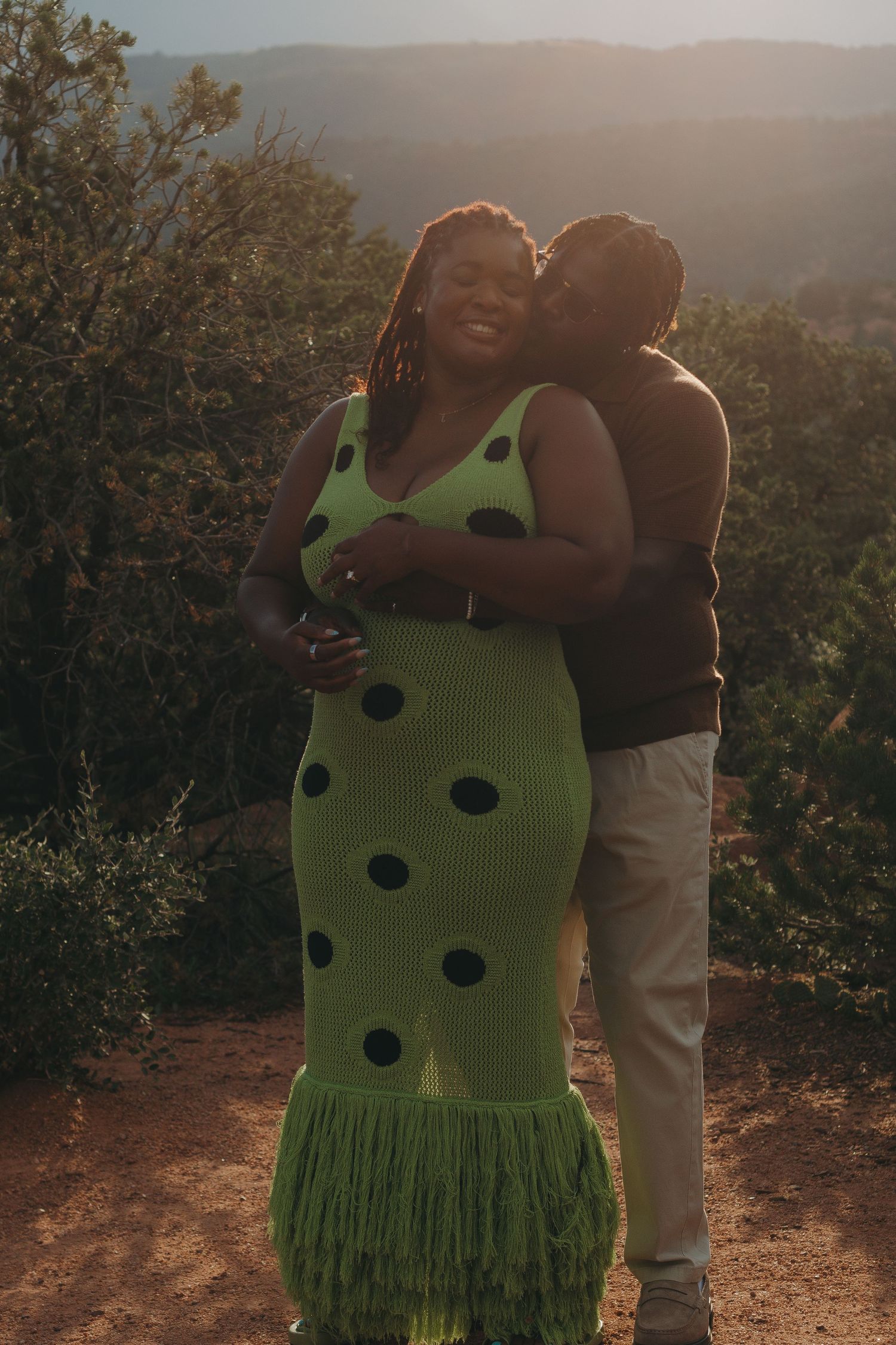 A tender moment captured at sunset with mountains and greenery in the background.
