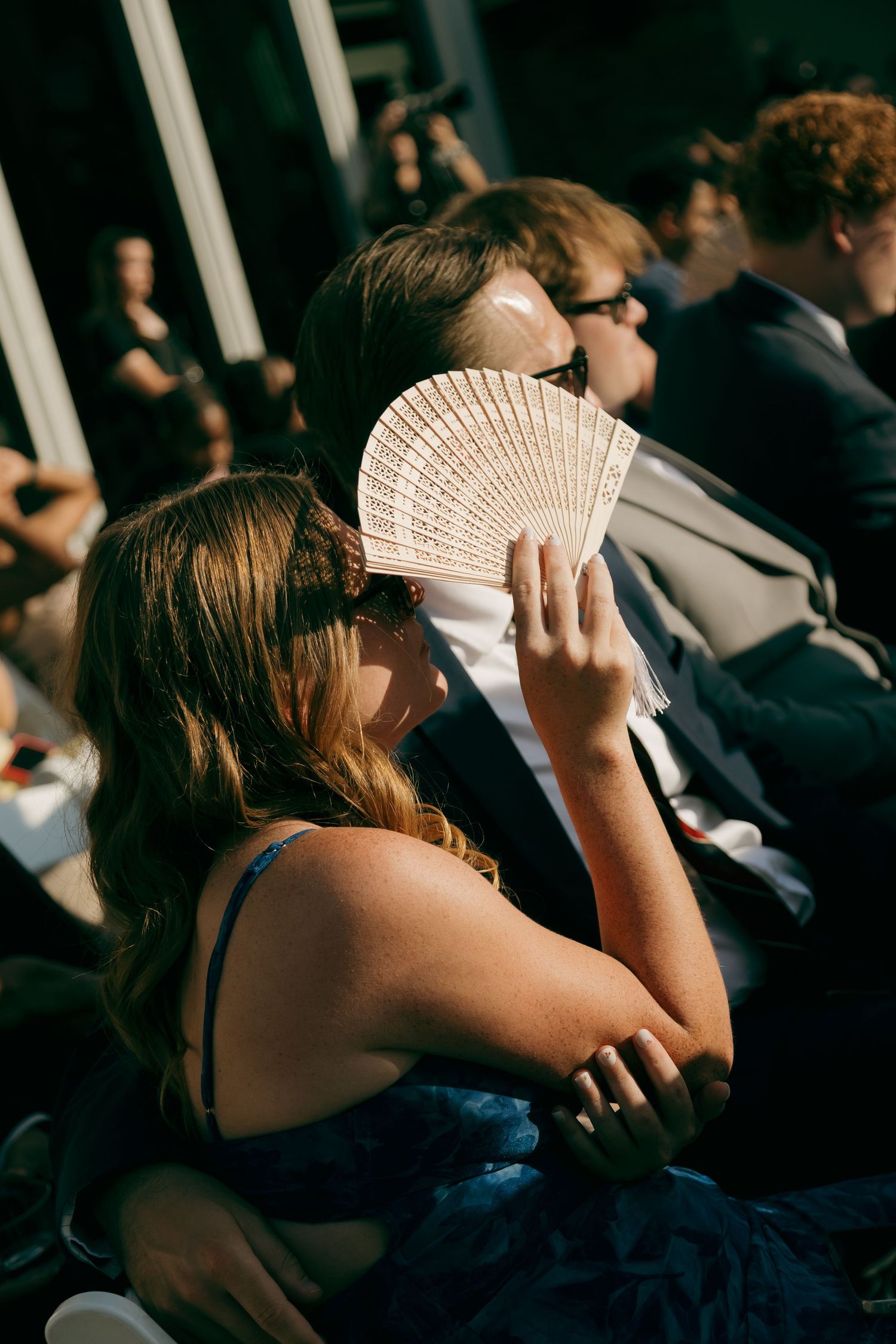 Wedding guest using decorative hand fan to stay cool during outdoor ceremony.