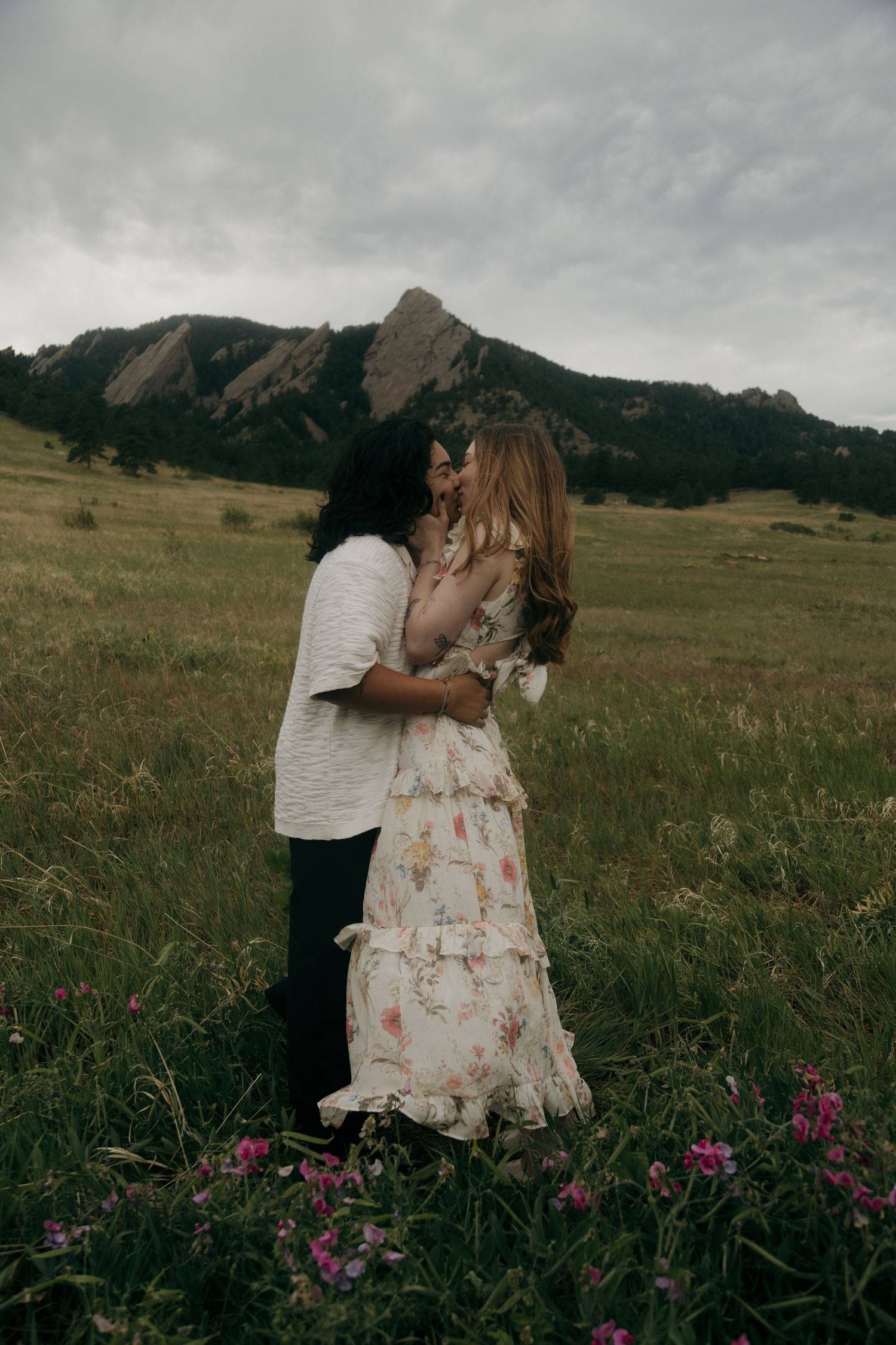 Couple kissing in a wildflower meadow with the iconic Flatirons rock formations of Boulder, Colorado behind them.