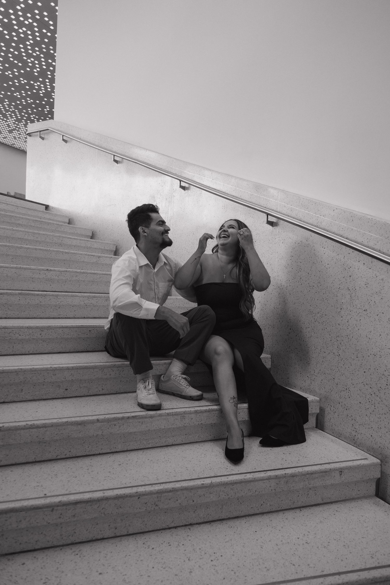 Couple sitting on marble steps laughing together in a black and white portrait.