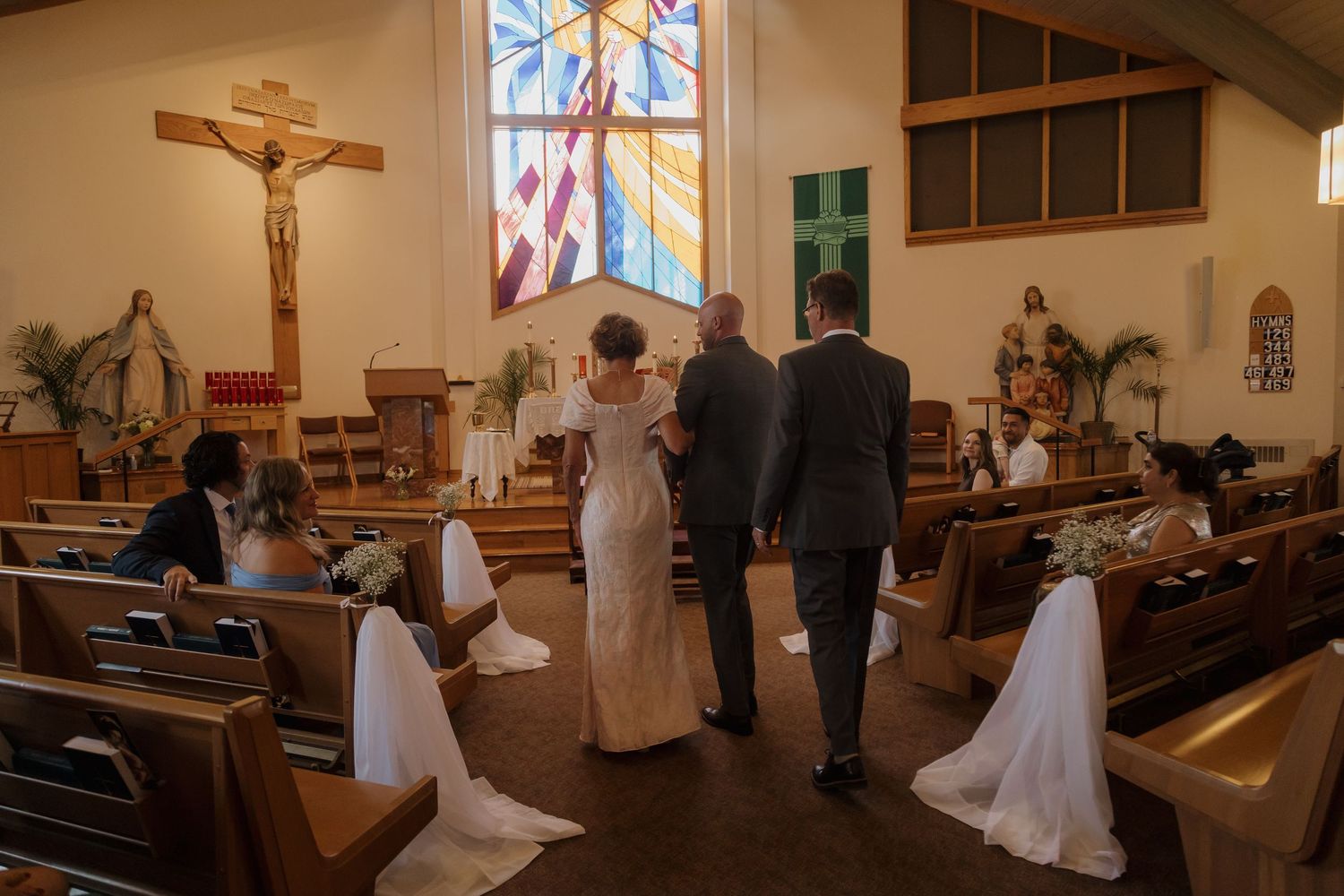Bride and groom stand at church altar during wedding ceremony with stained glass windows and wooden pews.
