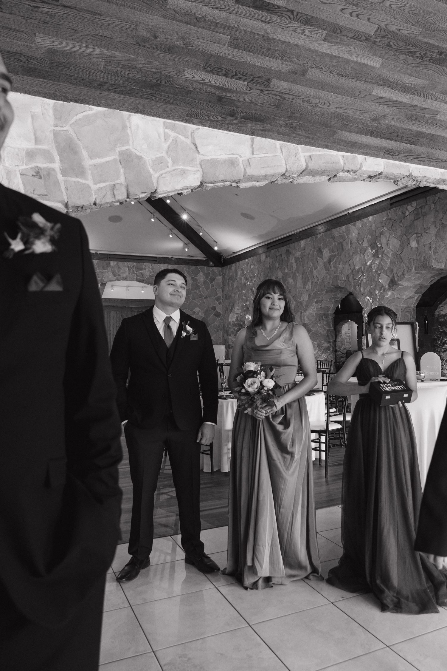 Black and white photo of groomsman and bridesmaids watching ceremony in elegant stone venue.