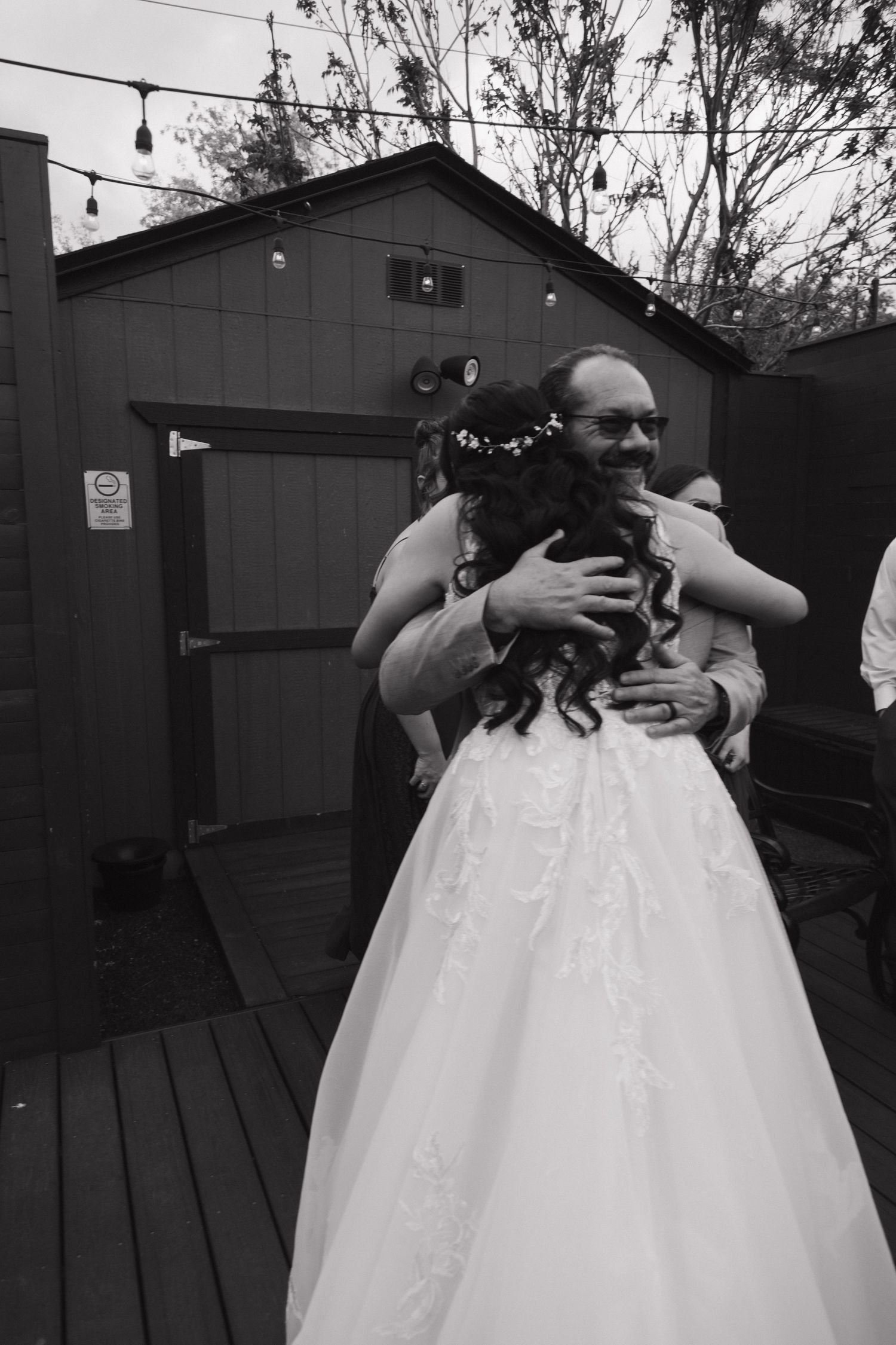 Black and white photo of groom joyfully hugging bride on outdoor deck at wedding reception.