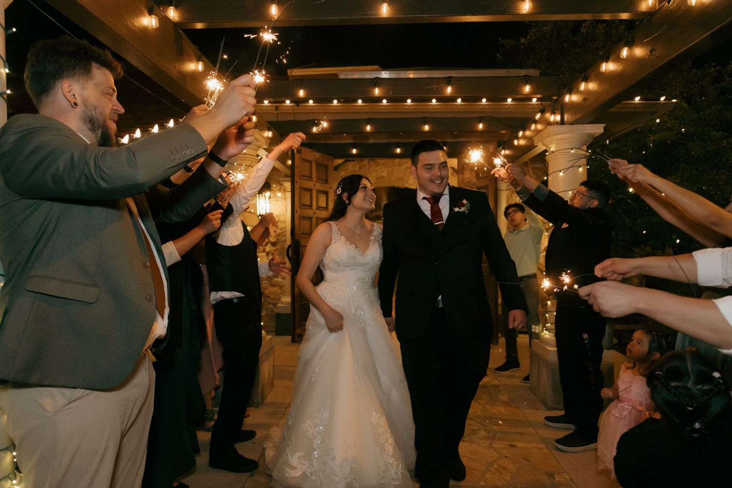 Bride and groom exit through sparkler tunnel surrounded by cheering guests at night wedding.