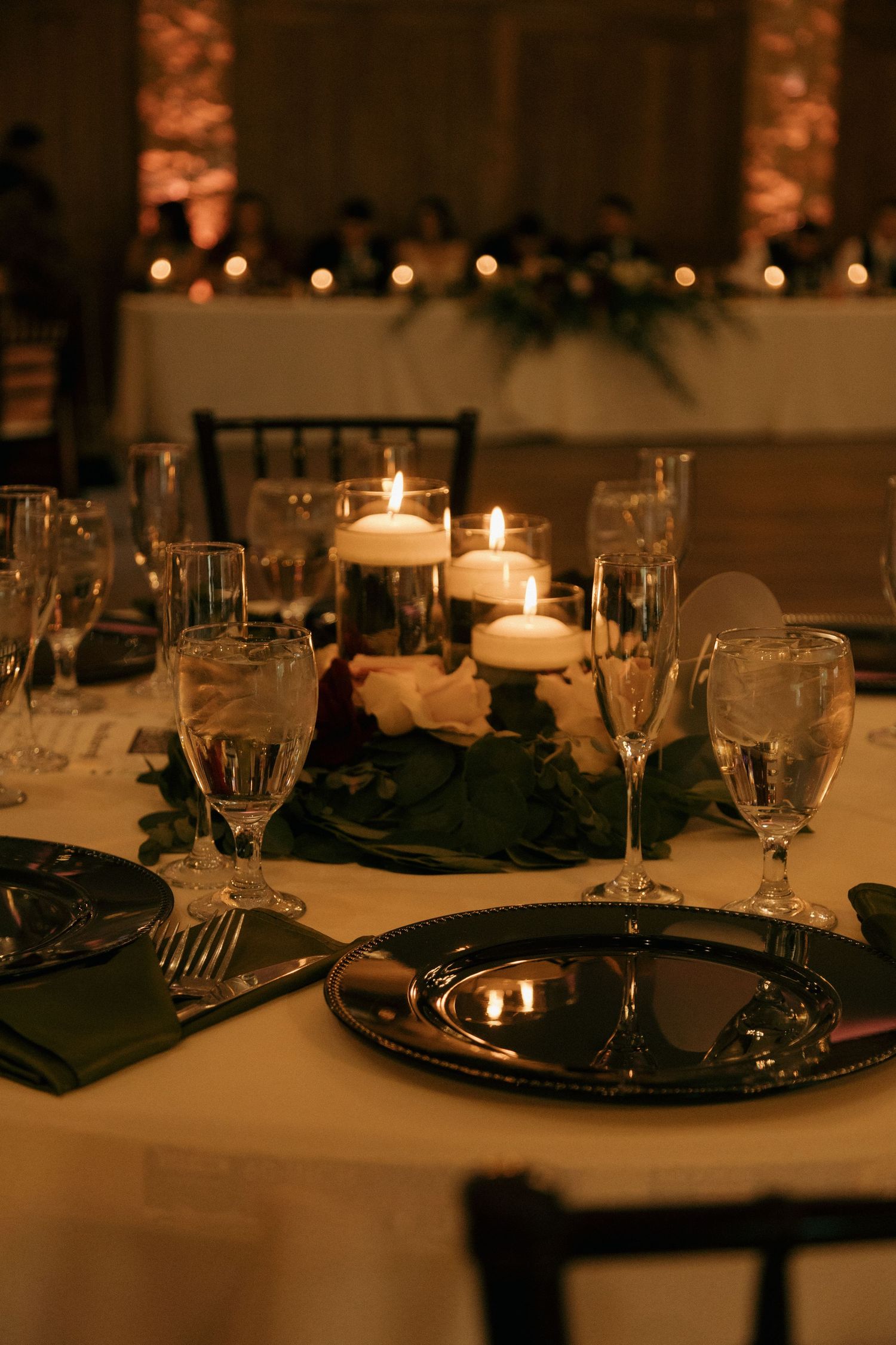 Elegant wedding reception table with pillar candles, green napkins, silver charger plates, and crystal glassware.