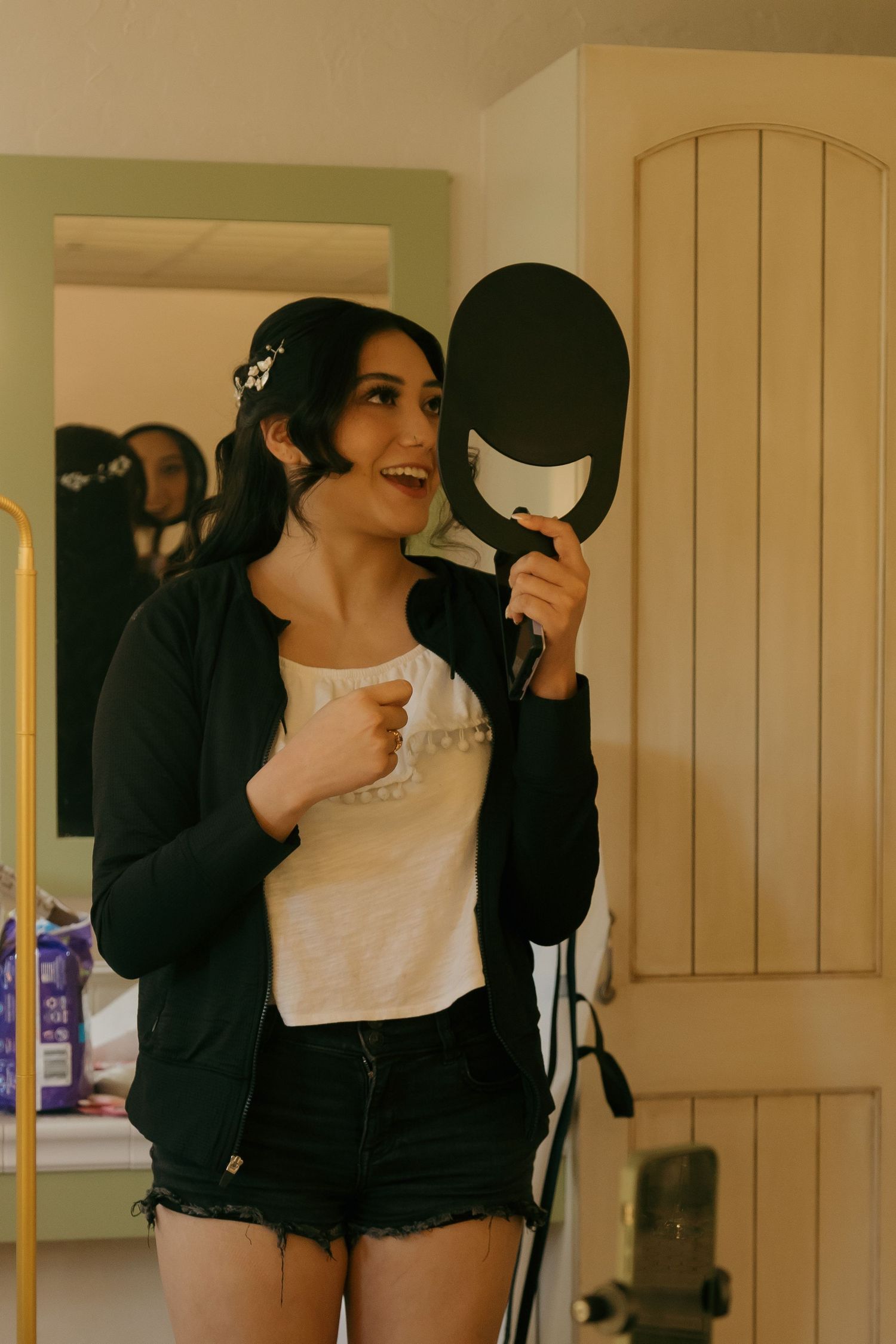 Bride smiling and holding a hand mirror while getting ready in a black hoodie and white top.